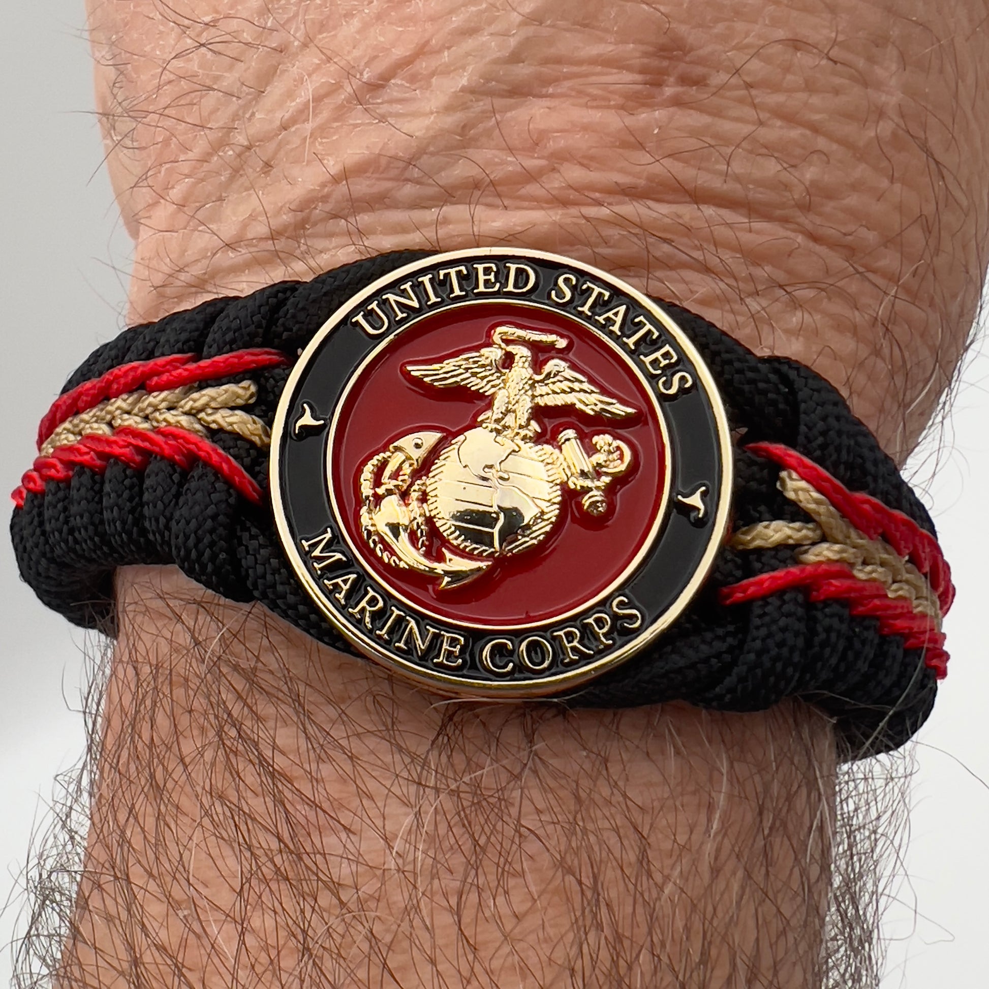 Thick, semi-rigid and comfortable braided United States Marine Corps bracelet featuring a 24K gold and silver plated USMC officer Eagle Globe and Anchor medallion, a black Cobra style tactical buckle and woven with black 550, Imperial red and gold micro paracord.