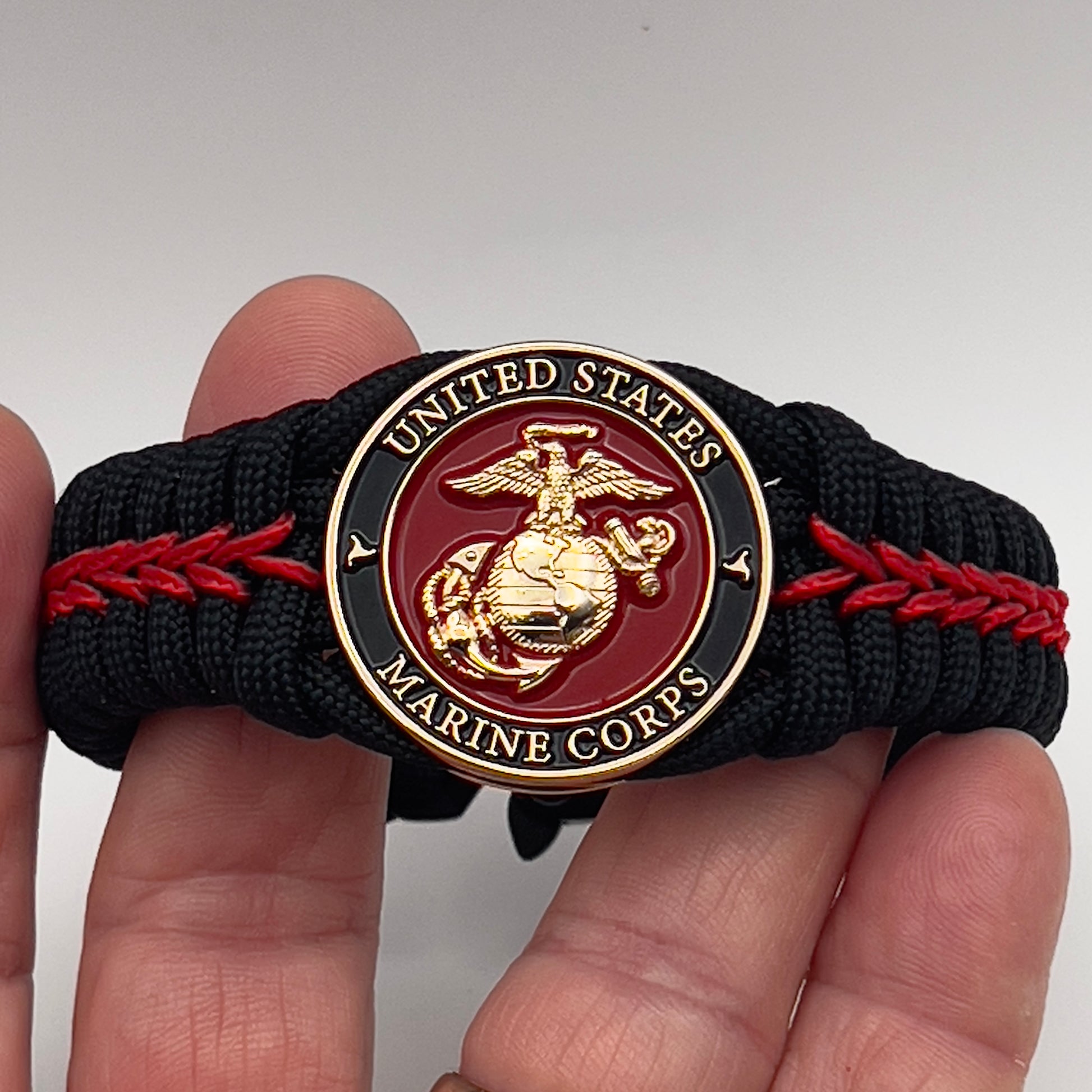 Thick, semi-rigid and comfortable braided United States Marine Corps bracelet featuring a 24K gold plated USMC officer Eagle Globe and Anchor medallion, a black Cobra style tactical buckle and woven with black 550 paracord and Imperial Red micro cord.