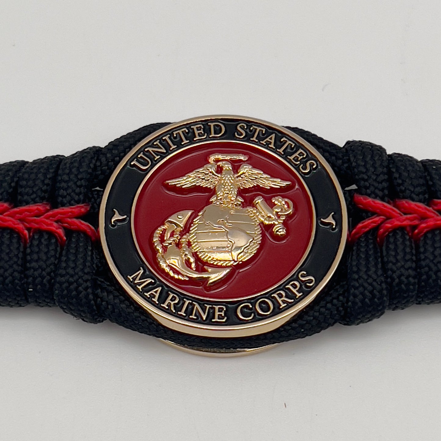 Thick, semi-rigid and comfortable braided United States Marine Corps bracelet featuring a 24K gold plated USMC officer Eagle Globe and Anchor medallion, a black Cobra style tactical buckle and woven with black 550 paracord and Imperial Red micro cord.