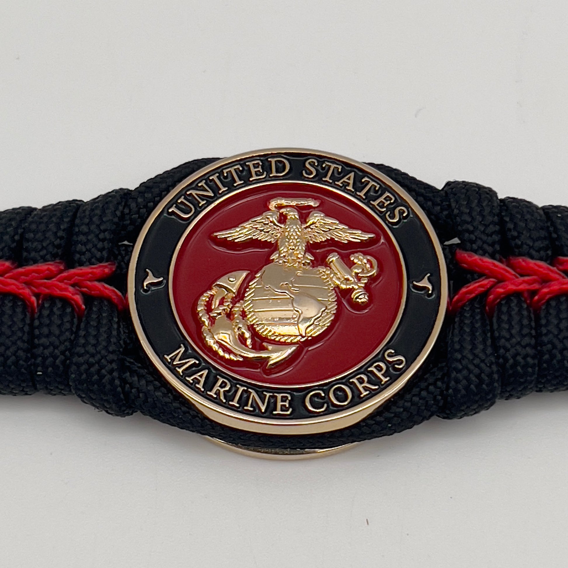 Thick, semi-rigid and comfortable braided United States Marine Corps bracelet featuring a 24K gold plated USMC officer Eagle Globe and Anchor medallion, a black Cobra style tactical buckle and woven with black 550 paracord and Imperial Red micro cord.