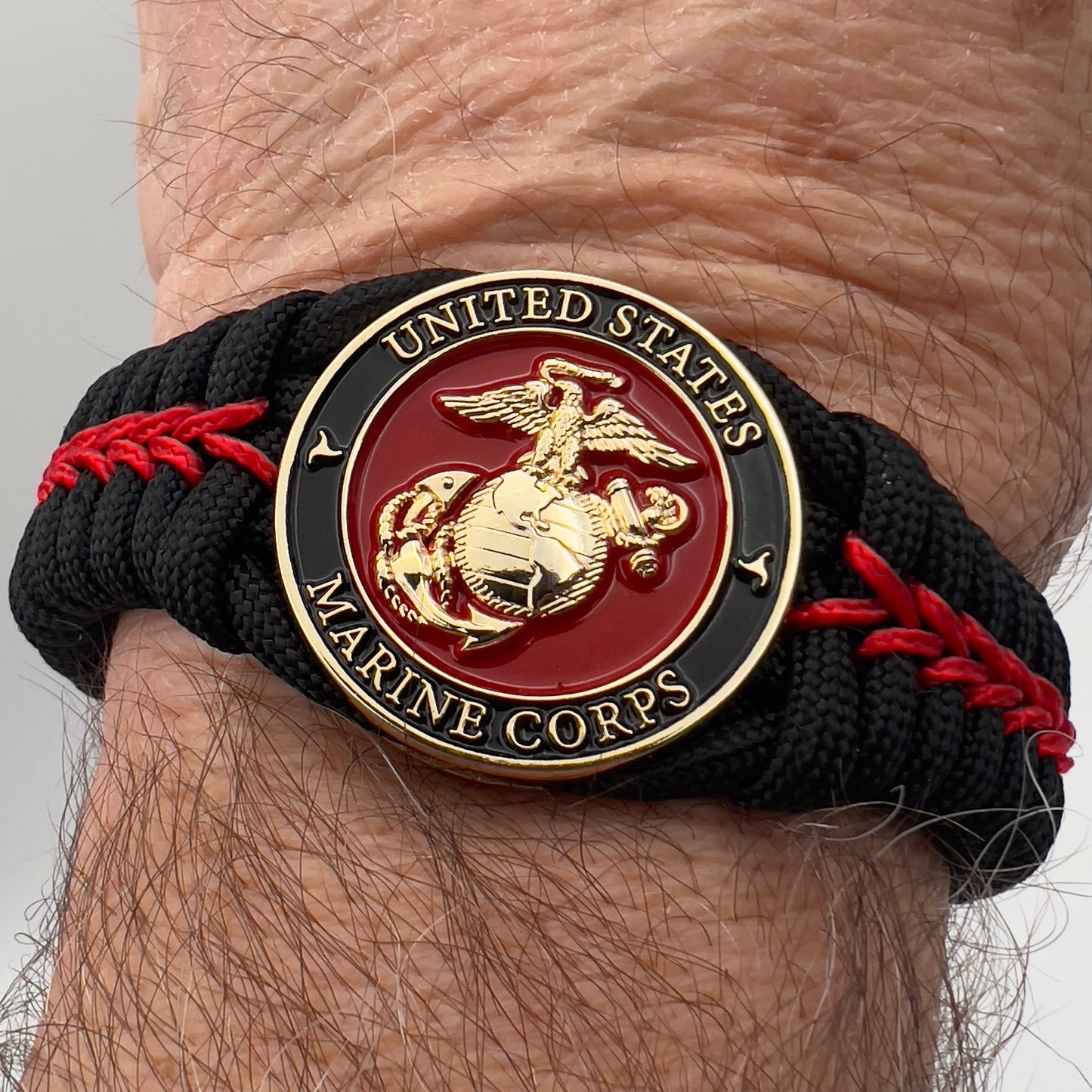 Thick, semi-rigid and comfortable braided United States Marine Corps bracelet featuring a 24K gold plated USMC officer Eagle Globe and Anchor medallion, a black Cobra style tactical buckle and woven with black 550 paracord and Imperial Red micro cord.