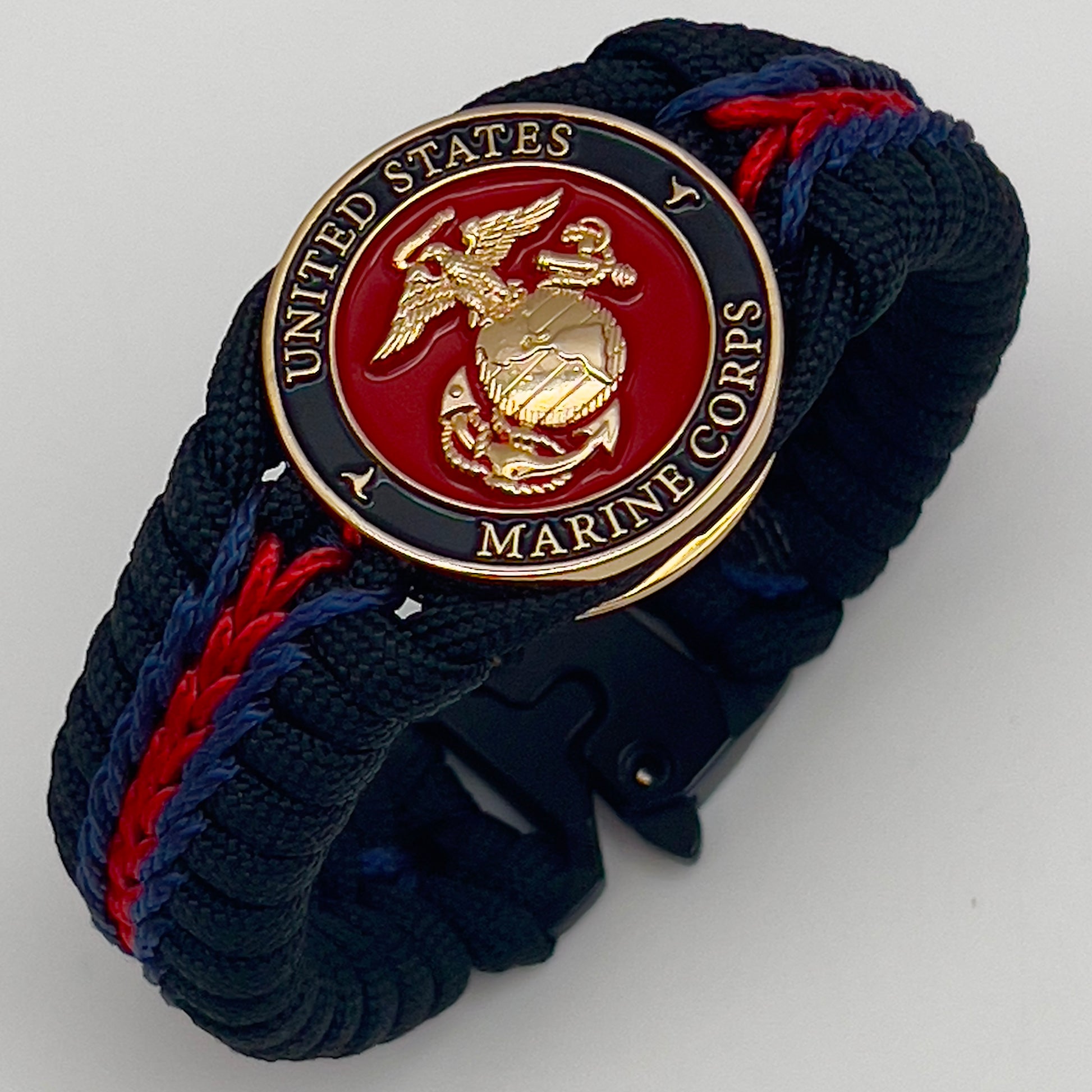Thick, rigid and comfortable braided United States Marine Corps bracelet featuring a 24K gold plated USMC officer Eagle Globe and Anchor medallion, a black Cobra style tactical buckle and woven with black 550, Imperial red and Navy Blue micro paracord.