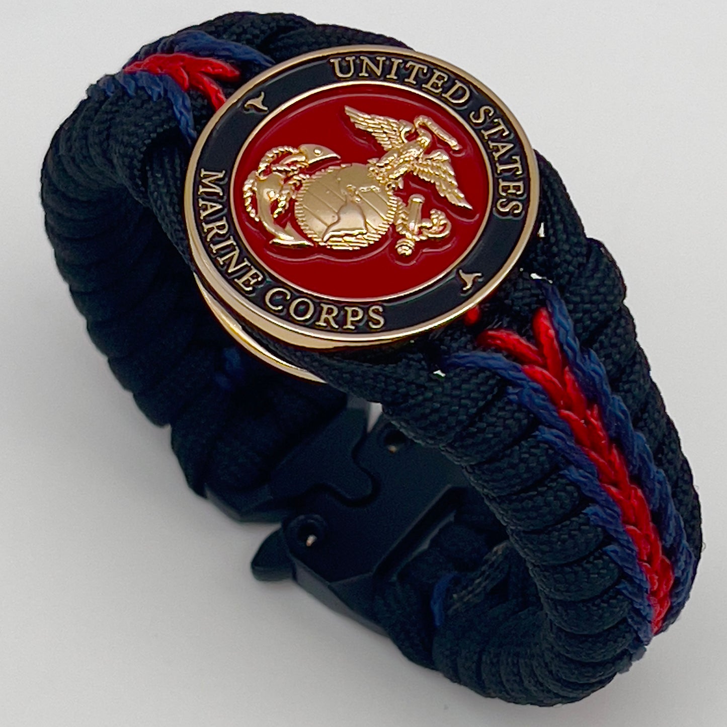 Thick, rigid and comfortable braided United States Marine Corps bracelet featuring a 24K gold plated USMC officer Eagle Globe and Anchor medallion, a black Cobra style tactical buckle and woven with black 550, Imperial red and Navy Blue micro paracord.