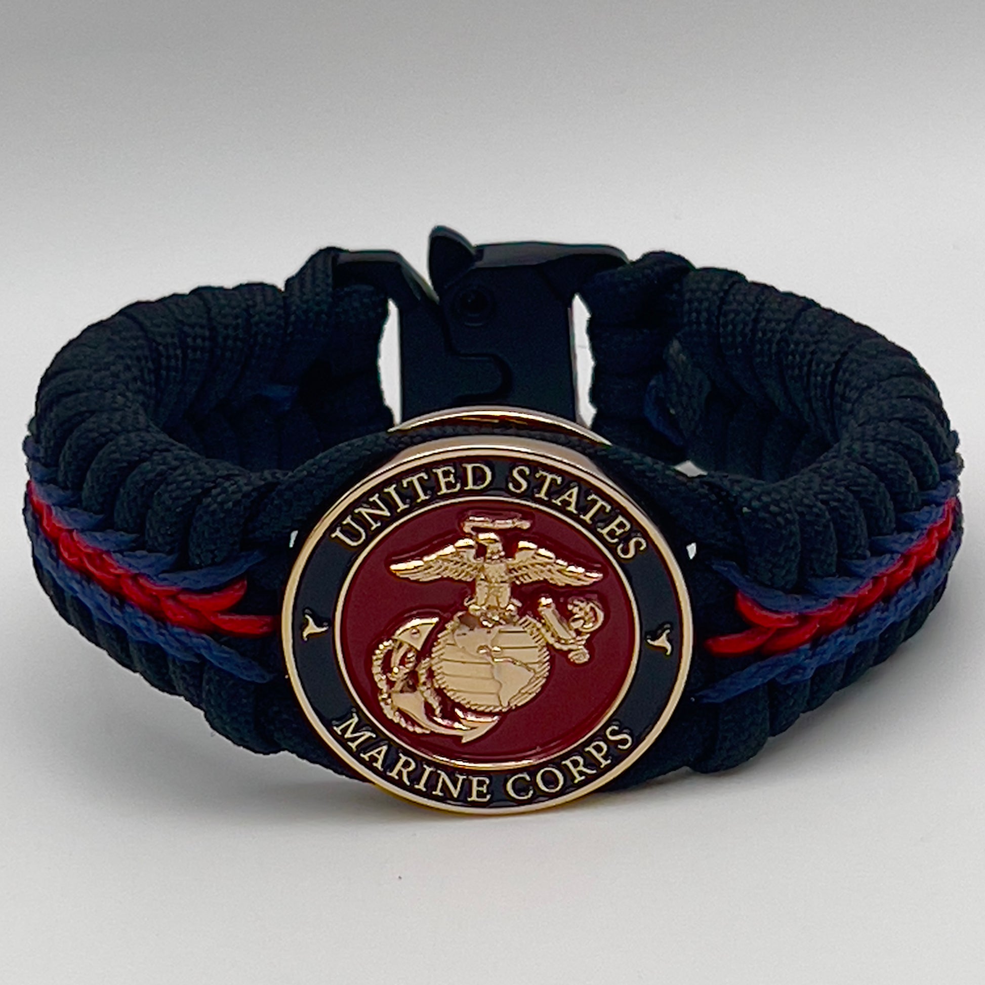 Thick, rigid and comfortable braided United States Marine Corps bracelet featuring a 24K gold plated USMC officer Eagle Globe and Anchor medallion, a black Cobra style tactical buckle and woven with black 550, Imperial red and Navy Blue micro paracord.
