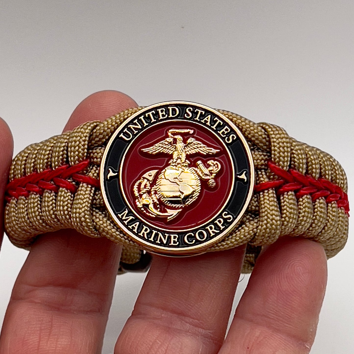 Thick, semi-rigid and comfortable braided United States Marine Corps bracelet featuring a 24K gold plated USMC officer Eagle Globe and Anchor medallion, a gold Cobra style tactical buckle and woven with gold 550 paracord and Imperial Red micro cord.