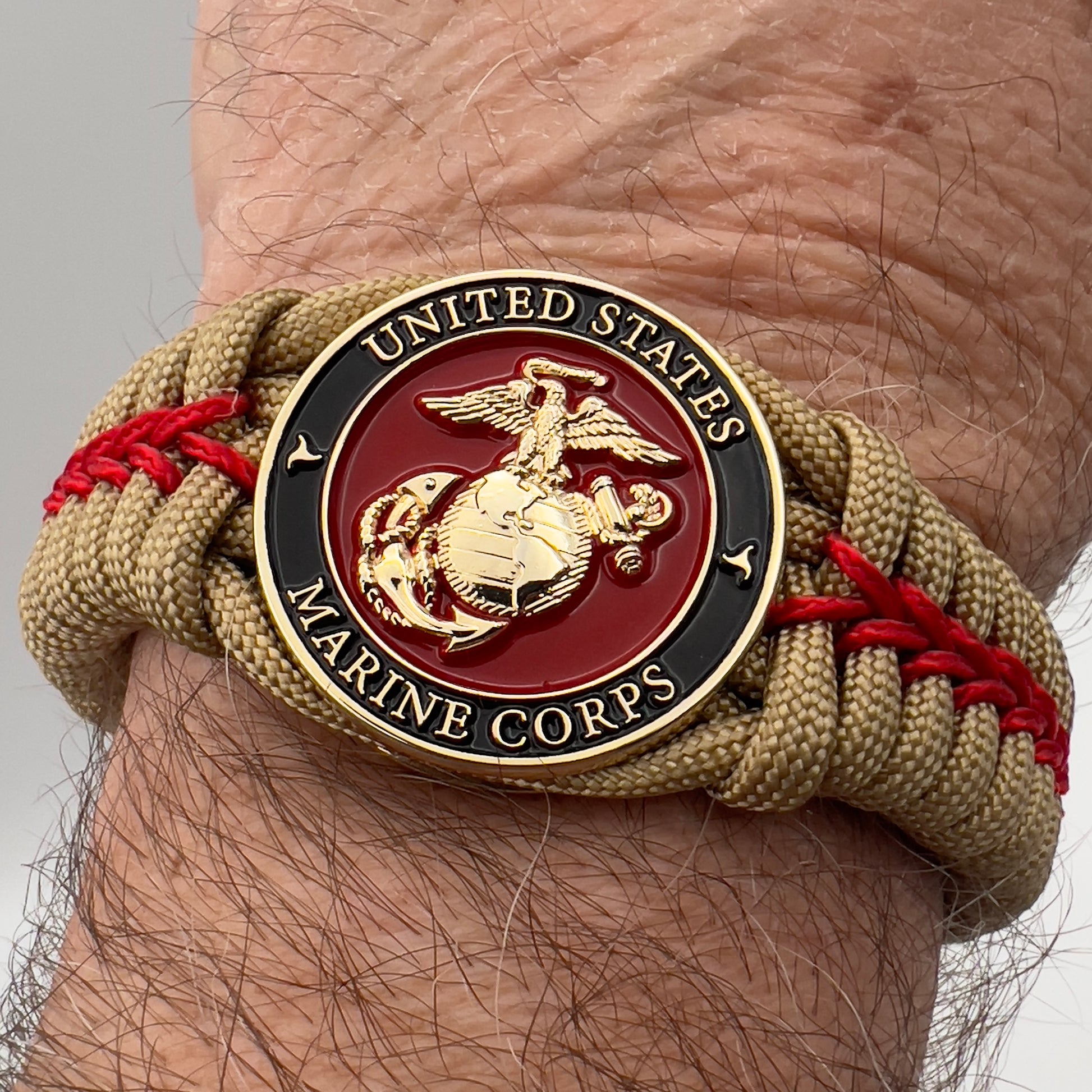 Thick, semi-rigid and comfortable braided United States Marine Corps bracelet featuring a 24K gold plated USMC officer Eagle Globe and Anchor medallion, a gold Cobra style tactical buckle and woven with gold 550 paracord and Imperial Red micro cord.