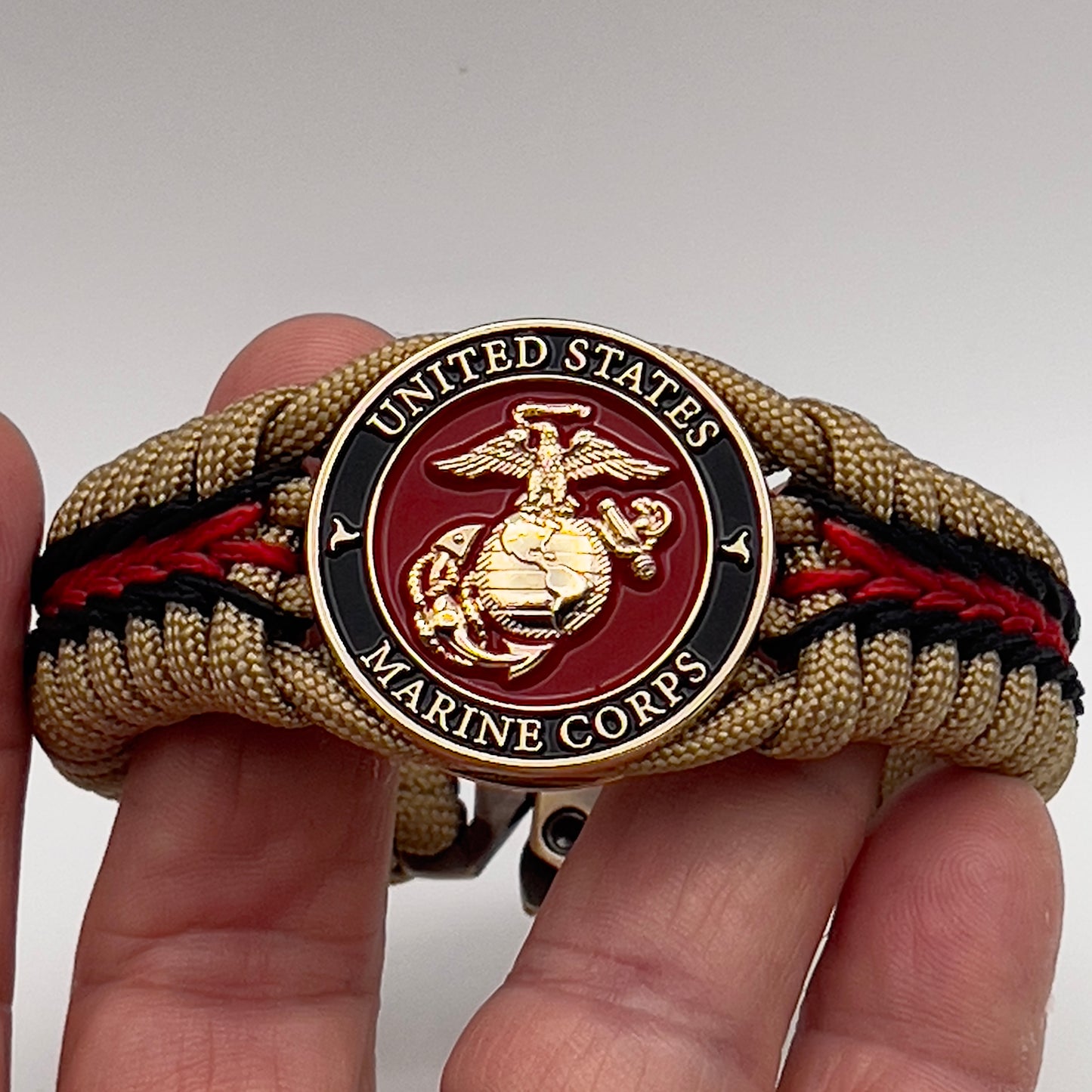 Thick, rigid and comfortable braided United States Marine Corps bracelet featuring a 24K gold plated USMC officer Eagle Globe and Anchor medallion, a gold Cobra style tactical buckle and woven with gold 550 paracord and Imperial Red and black micro cord.
