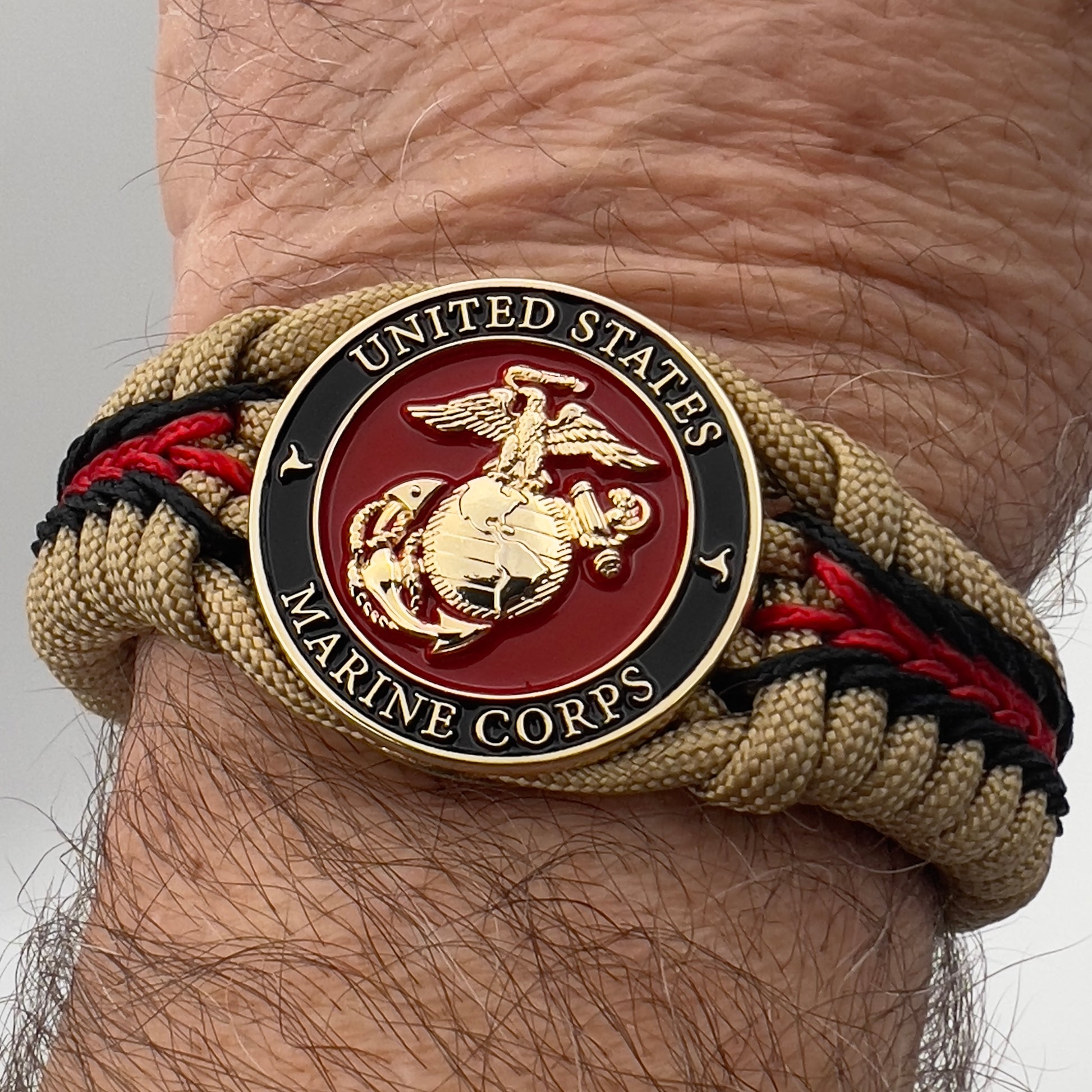 Thick, rigid and comfortable braided United States Marine Corps bracelet featuring a 24K gold plated USMC officer Eagle Globe and Anchor medallion, a gold Cobra style tactical buckle and woven with gold 550 paracord and Imperial Red and black micro cord.