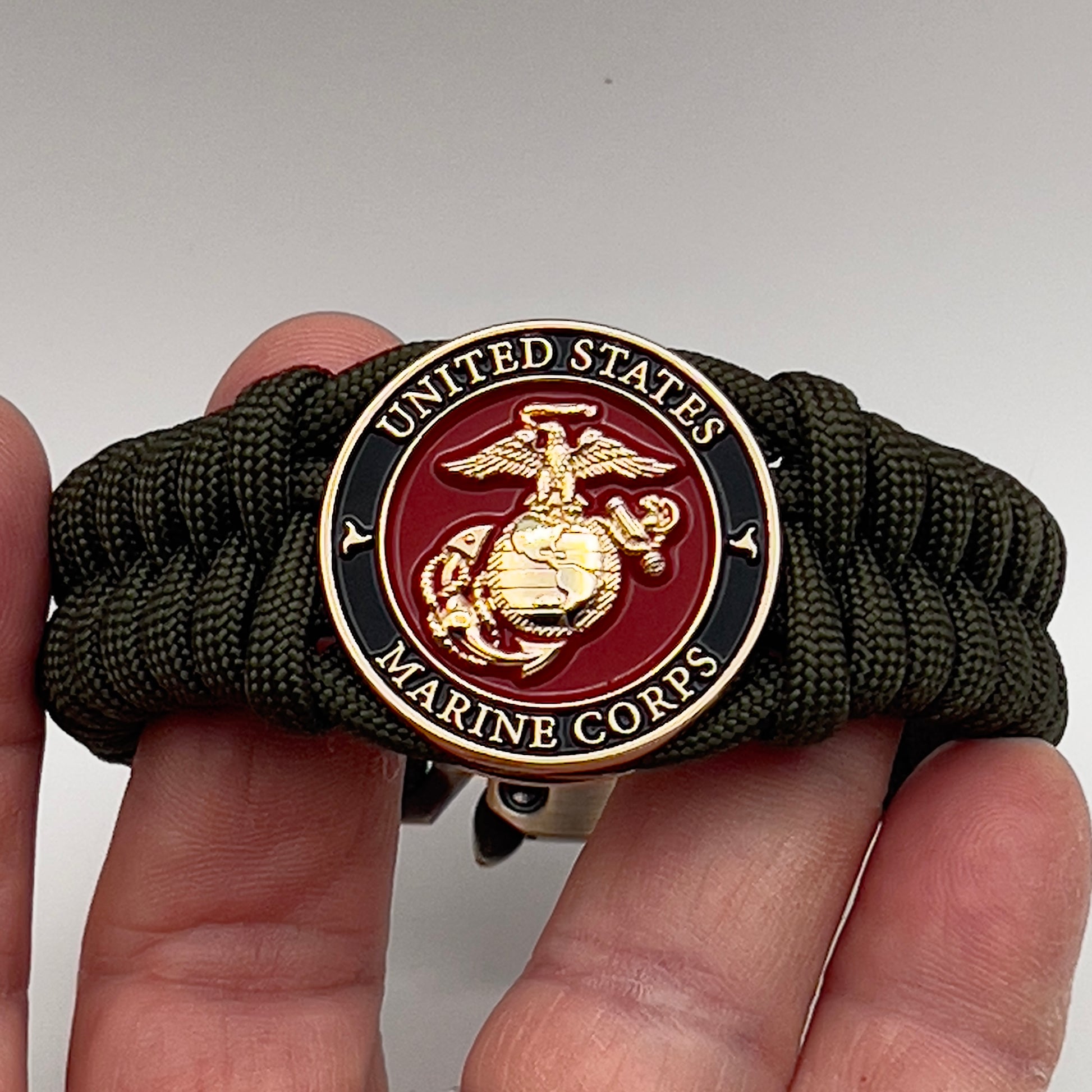 Thick, semi-rigid and comfortable braided United States Marine Corps bracelet featuring a 24K gold plated USMC officer Eagle Globe and Anchor medallion, a gold Cobra style tactical buckle and woven with olive drab 550 paracord.