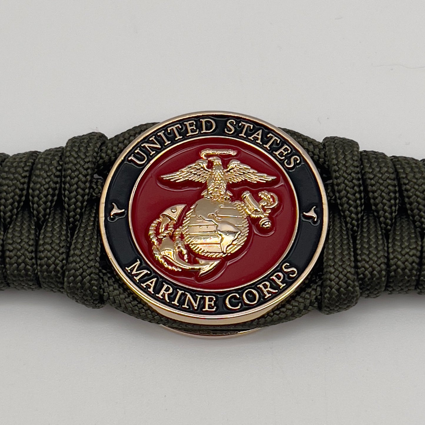 Thick, semi-rigid and comfortable braided United States Marine Corps bracelet featuring a 24K gold plated USMC officer Eagle Globe and Anchor medallion, a gold Cobra style tactical buckle and woven with olive drab 550 paracord.