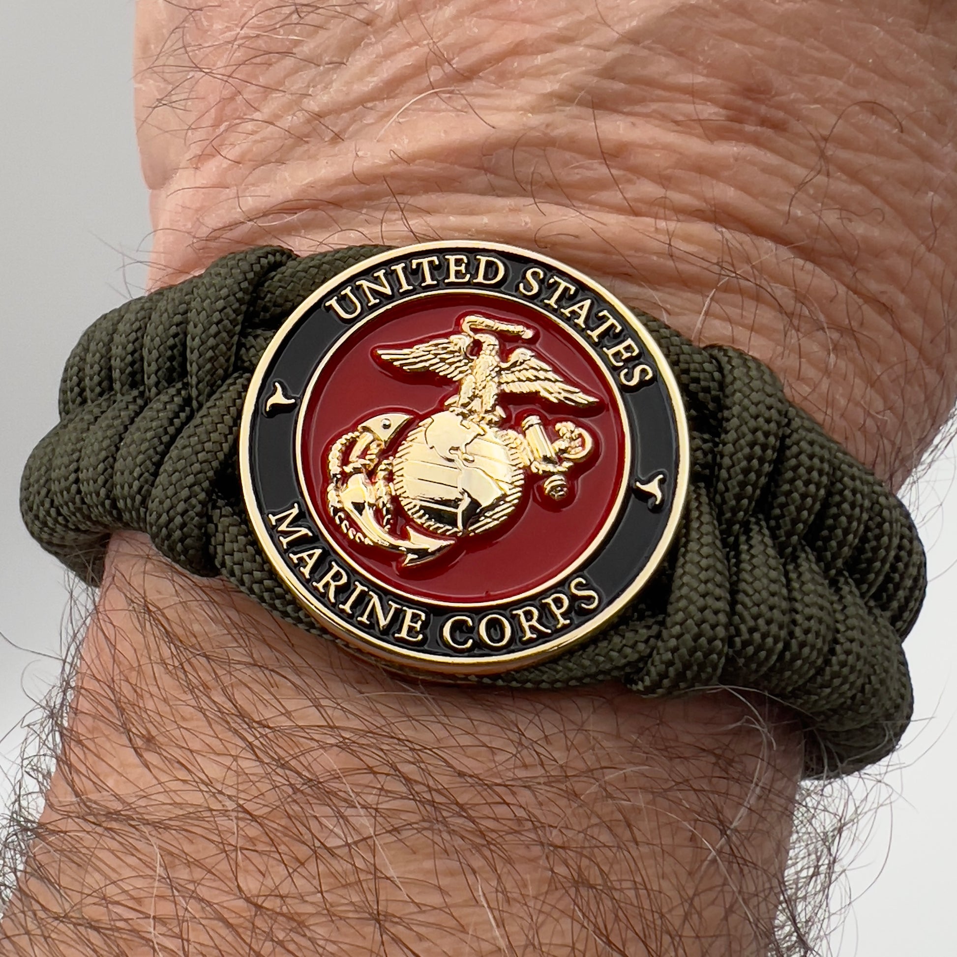 Thick, semi-rigid and comfortable braided United States Marine Corps bracelet featuring a 24K gold plated USMC officer Eagle Globe and Anchor medallion, a gold Cobra style tactical buckle and woven with olive drab 550 paracord.