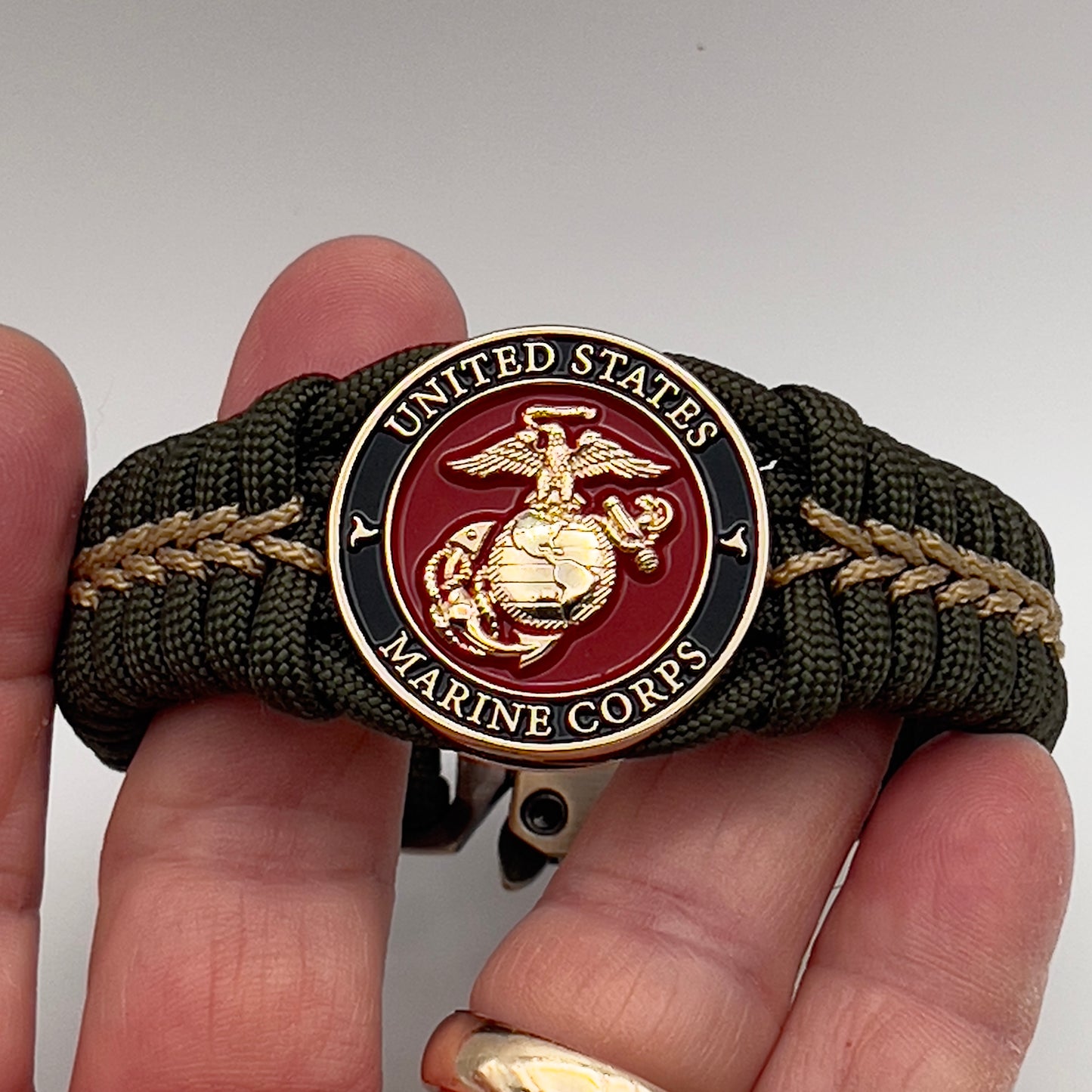 Thick, semi-rigid and comfortable braided United States Marine Corps bracelet featuring a 24K gold plated USMC officer Eagle Globe and Anchor medallion, a gold Cobra style tactical buckle and woven with olive drab 550 paracord and gold micro cord.