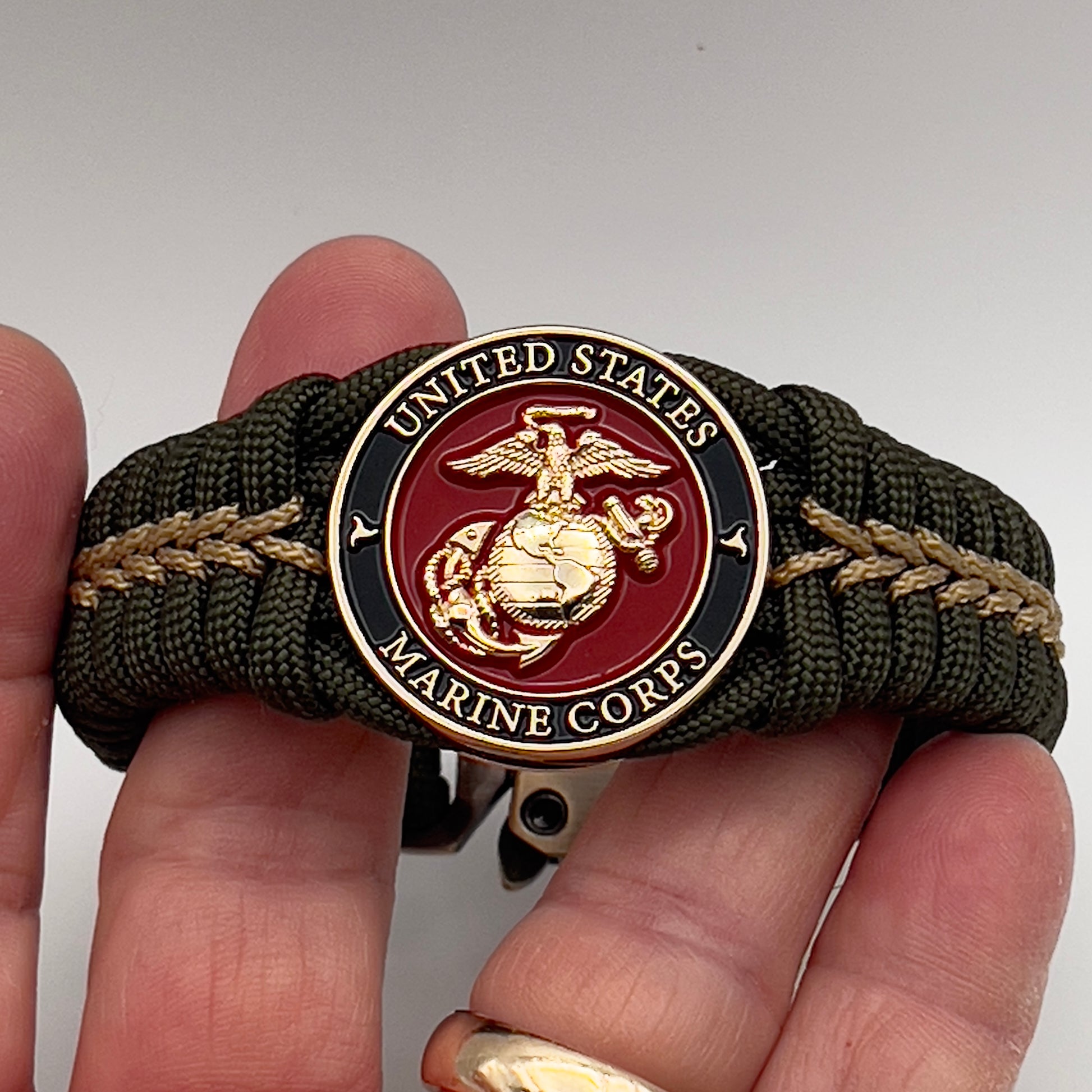 Thick, semi-rigid and comfortable braided United States Marine Corps bracelet featuring a 24K gold plated USMC officer Eagle Globe and Anchor medallion, a gold Cobra style tactical buckle and woven with olive drab 550 paracord and gold micro cord.