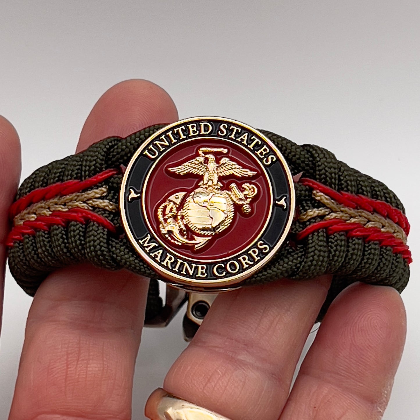 Thick, rigid and comfortable braided United States Marine Corps bracelet featuring a 24K gold plated USMC officer Eagle Globe and Anchor medallion, a gold Cobra style tactical buckle and woven with olive drab 550 paracord and Imperial Red and gold micro cord.