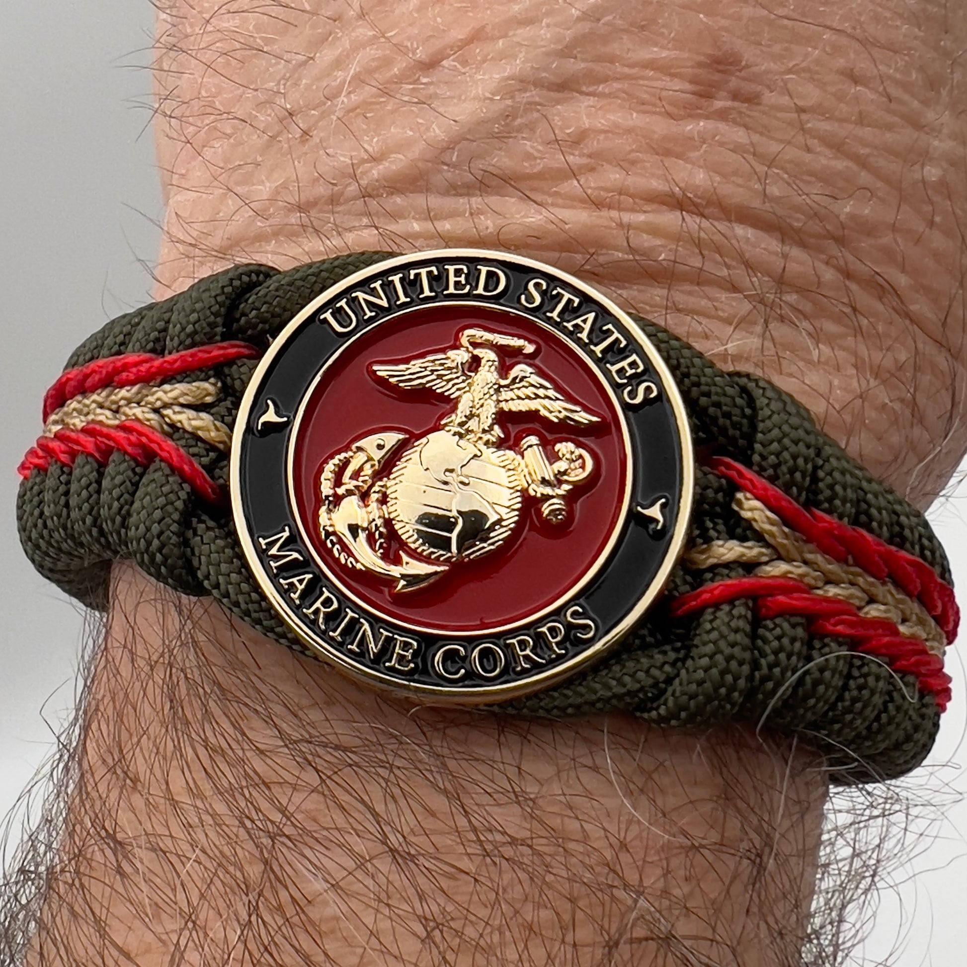 Thick, rigid and comfortable braided United States Marine Corps bracelet featuring a 24K gold plated USMC officer Eagle Globe and Anchor medallion, a gold Cobra style tactical buckle and woven with olive drab 550 paracord and Imperial Red and gold micro cord.