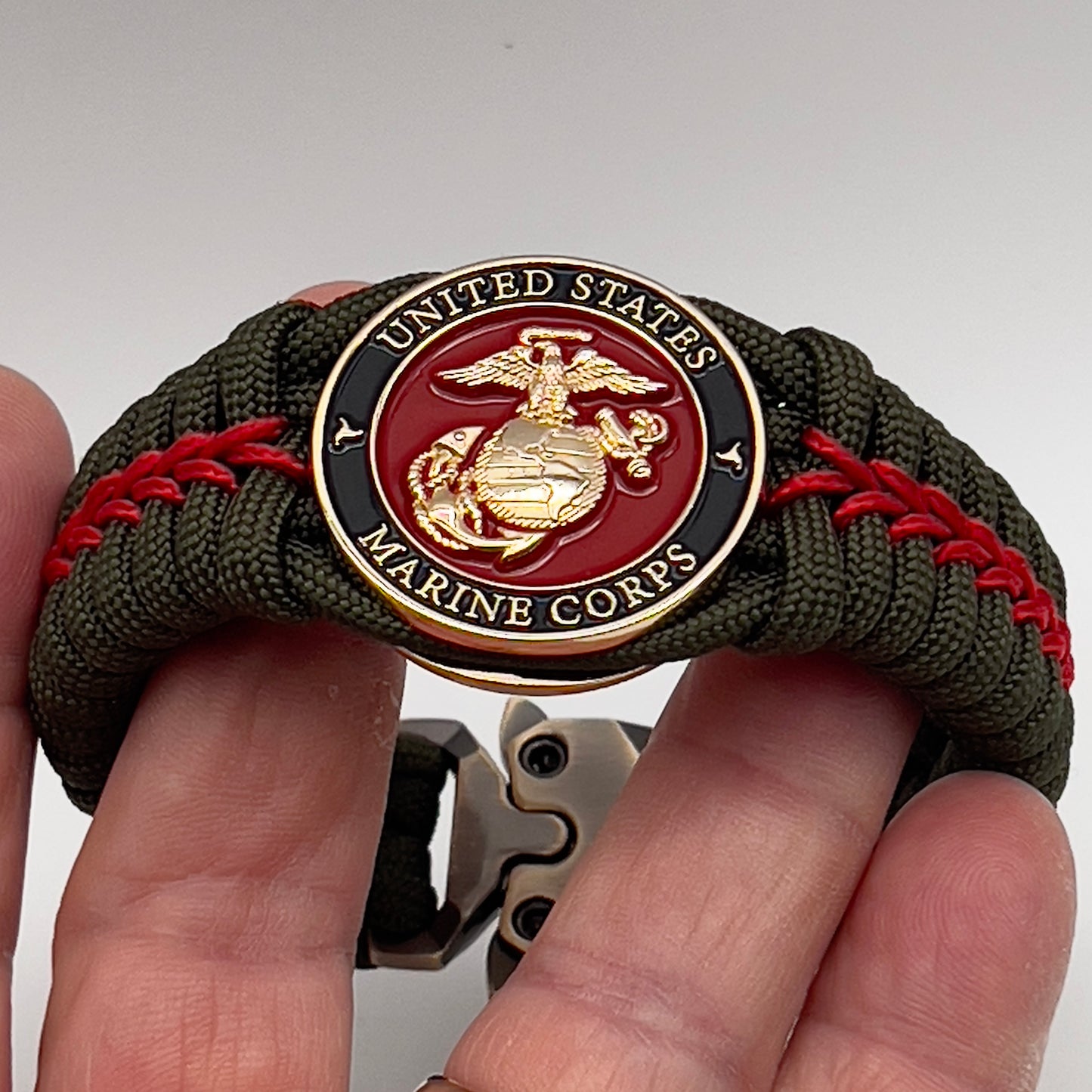 Thick, semi-rigid and comfortable braided United States Marine Corps bracelet featuring a 24K gold plated USMC officer Eagle Globe and Anchor medallion, a gold Cobra style tactical buckle and woven with olive drab 550 paracord and Imperial Red micro cord.