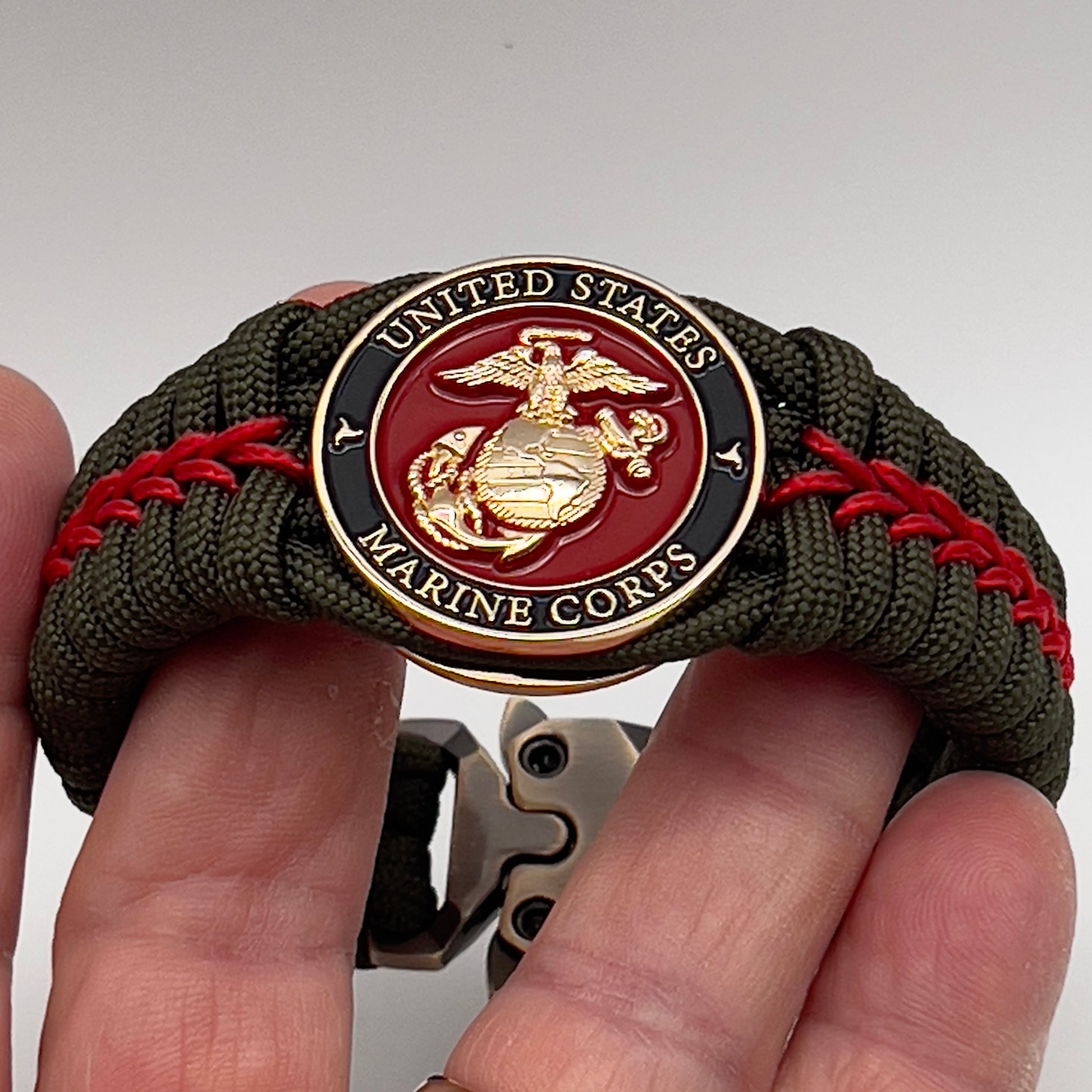 Thick, semi-rigid and comfortable braided United States Marine Corps bracelet featuring a 24K gold plated USMC officer Eagle Globe and Anchor medallion, a gold Cobra style tactical buckle and woven with olive drab 550 paracord and Imperial Red micro cord.