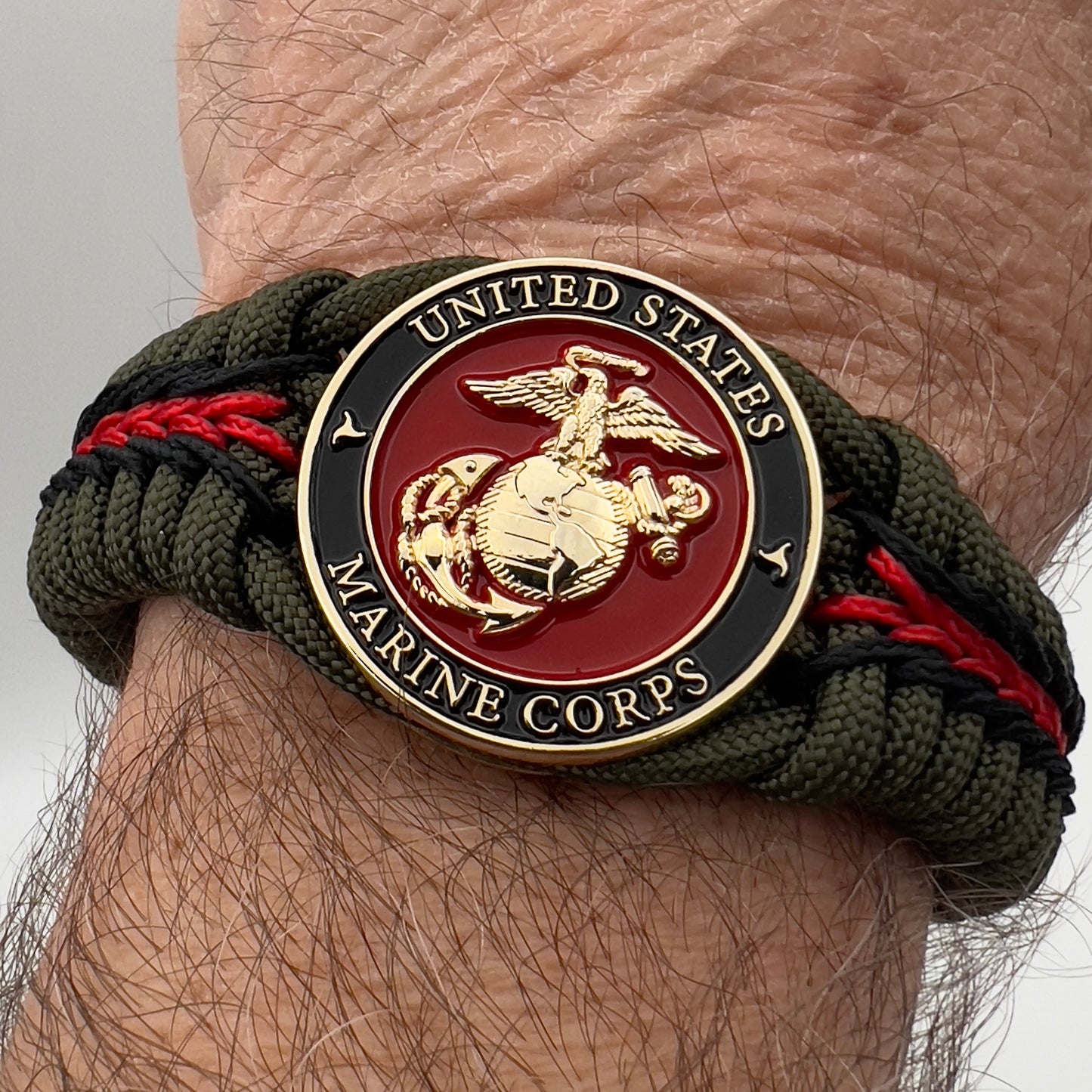 Thick, rigid and comfortable braided United States Marine Corps bracelet featuring a 24K gold plated USMC officer Eagle Globe and Anchor medallion, a gold Cobra style tactical buckle and woven with olive drab 550 paracord and black and Imperial red micro cord.