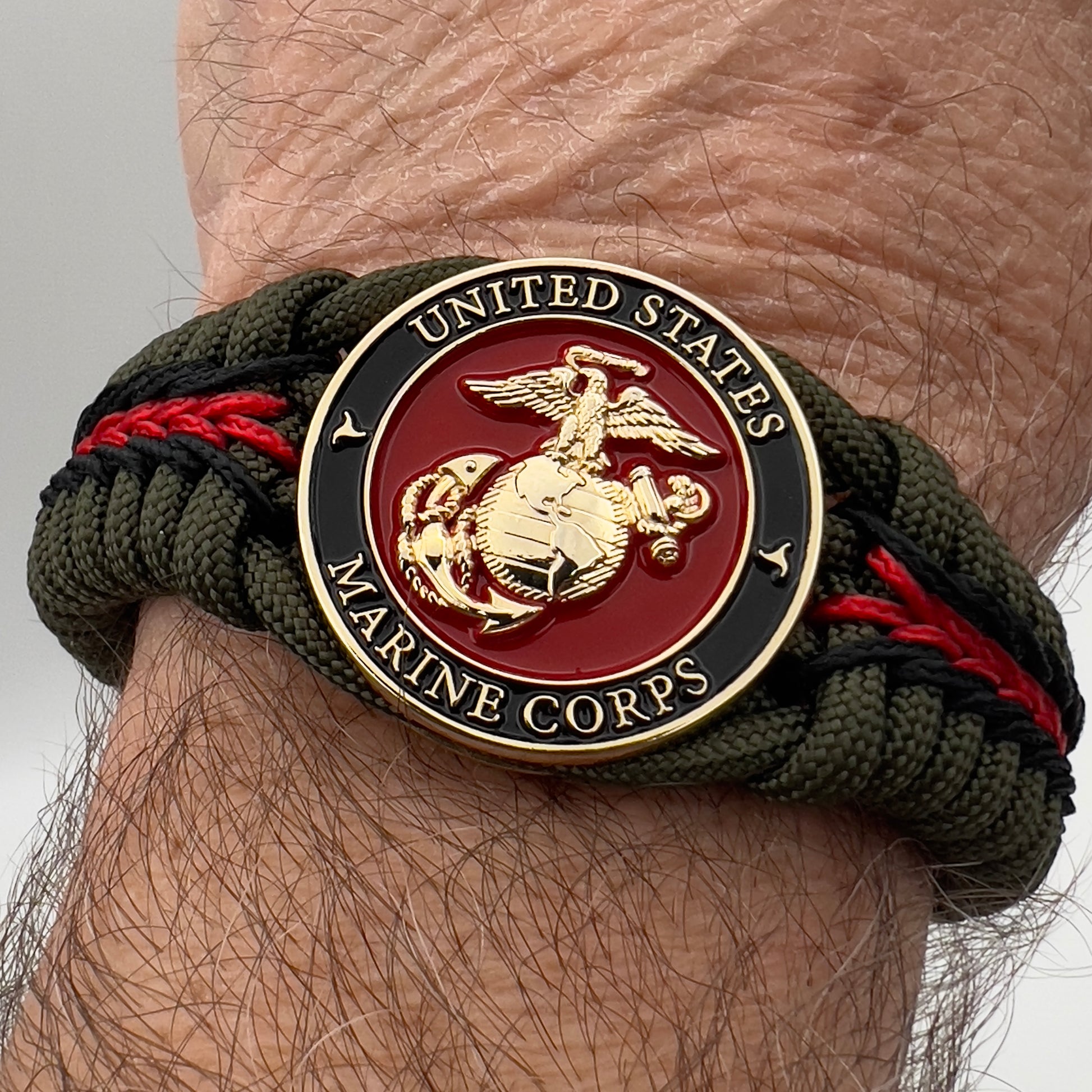 Thick, rigid and comfortable braided United States Marine Corps bracelet featuring a 24K gold plated USMC officer Eagle Globe and Anchor medallion, a gold Cobra style tactical buckle and woven with olive drab 550 paracord and black and Imperial red micro cord.