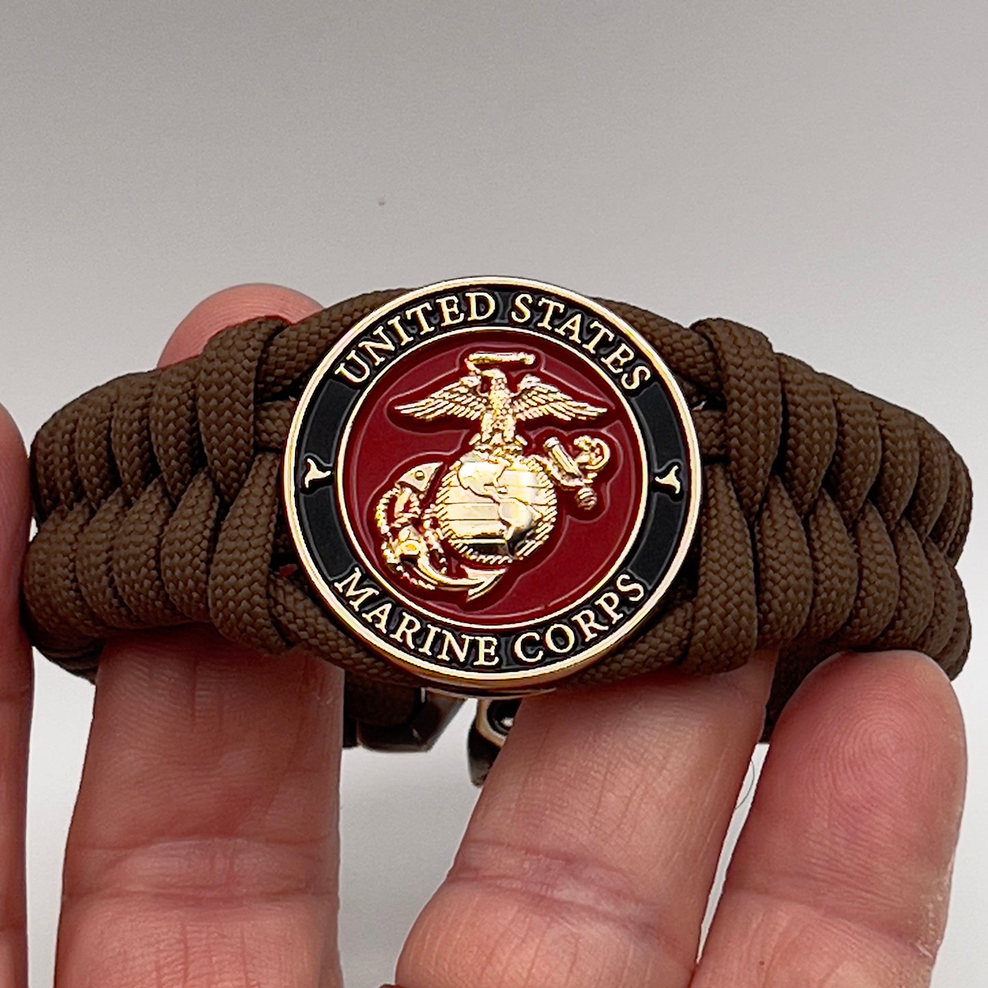Thick, semi-rigid and comfortable braided United States Marine Corps bracelet featuring a 24K gold plated USMC Eagle Globe and Anchor medallion, a gold Cobra style tactical buckle and woven with Coyote Brown 550 paracord.