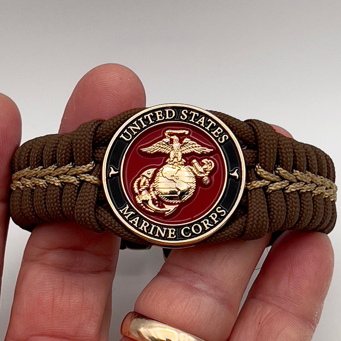 Thick, rigid and comfortable braided United States Marine Corps bracelet featuring a 24K gold plated USMC Eagle Globe and Anchor medallion, a gold Cobra style tactical buckle and woven with Coyote Brown 550 paracord and gold micro cord.