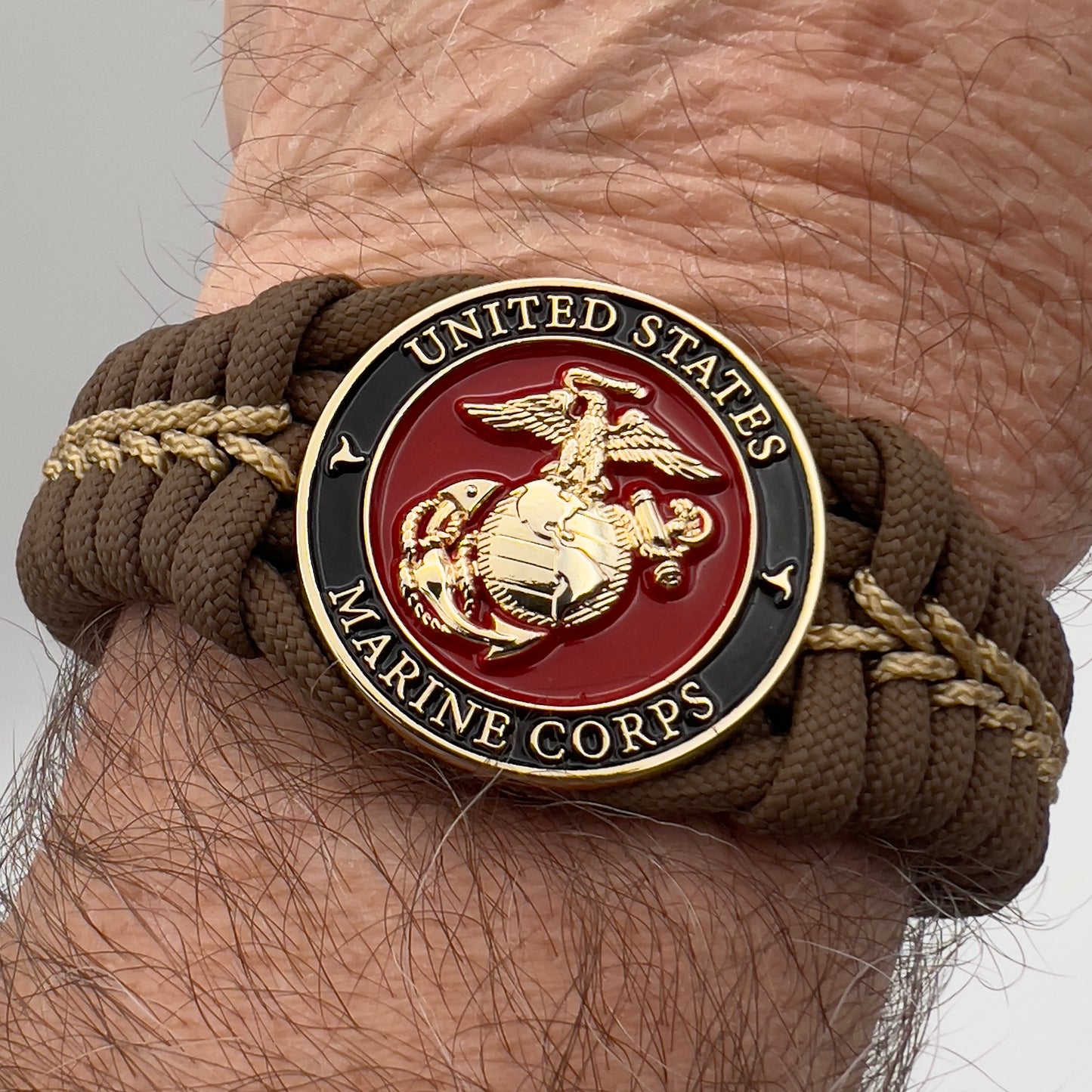 Thick, rigid and comfortable braided United States Marine Corps bracelet featuring a 24K gold plated USMC Eagle Globe and Anchor medallion, a gold Cobra style tactical buckle and woven with Coyote Brown 550 paracord and gold micro cord.
