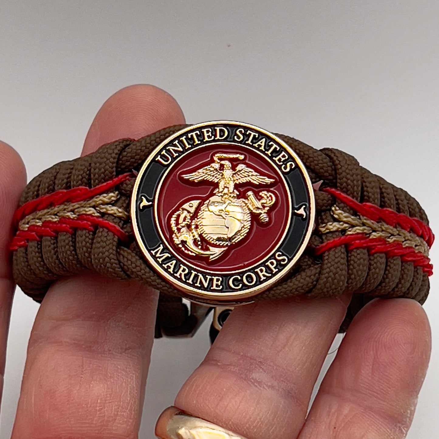 Thick, rigid and comfortable braided United States Marine Corps bracelet featuring a 24K gold plated USMC Eagle Globe and Anchor medallion, a gold Cobra style tactical buckle and woven with Coyote Brown 550 paracord and Imperial Red and gold micro cord.