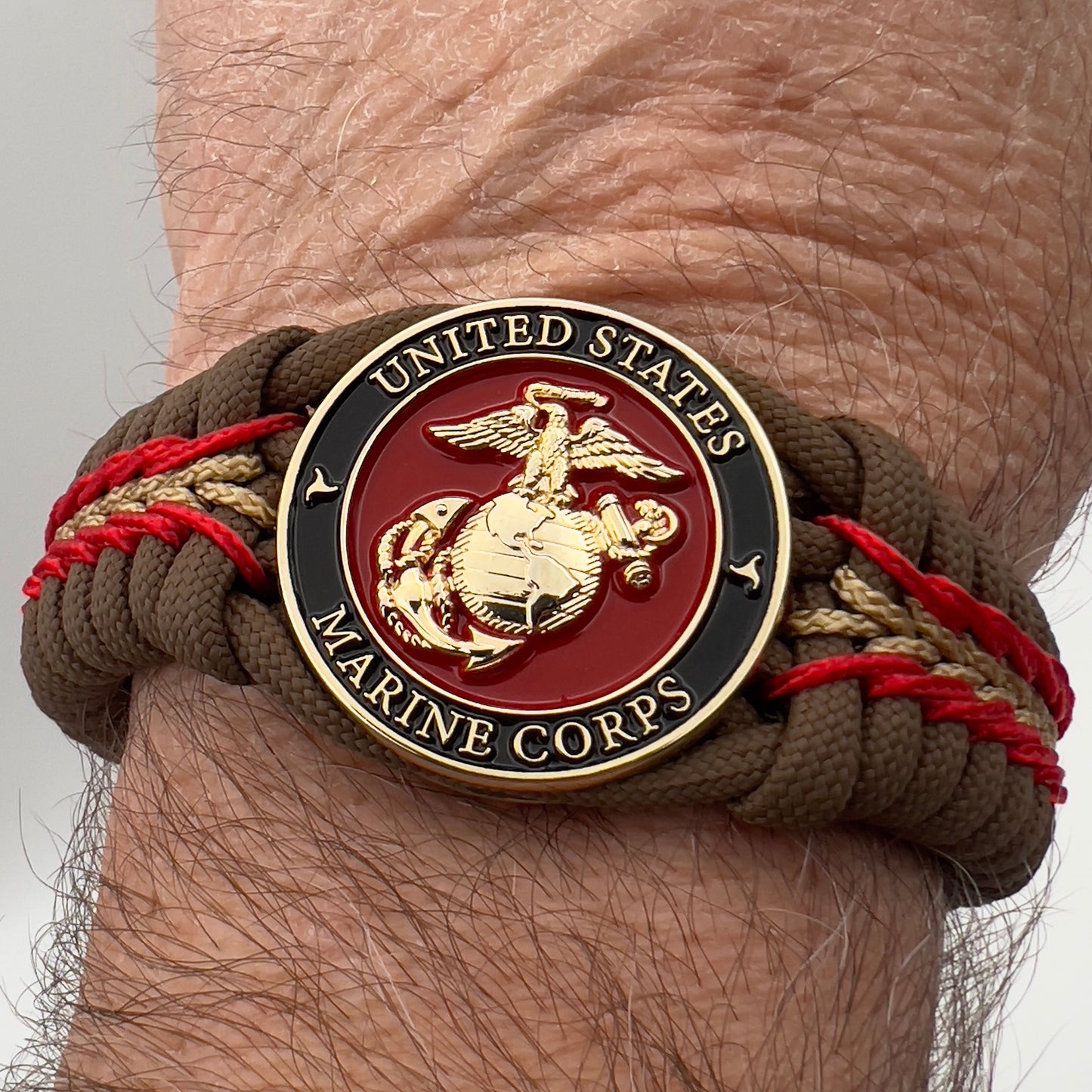 Thick, rigid and comfortable braided United States Marine Corps bracelet featuring a 24K gold plated USMC Eagle Globe and Anchor medallion, a gold Cobra style tactical buckle and woven with Coyote Brown 550 paracord and Imperial Red and gold micro cord.