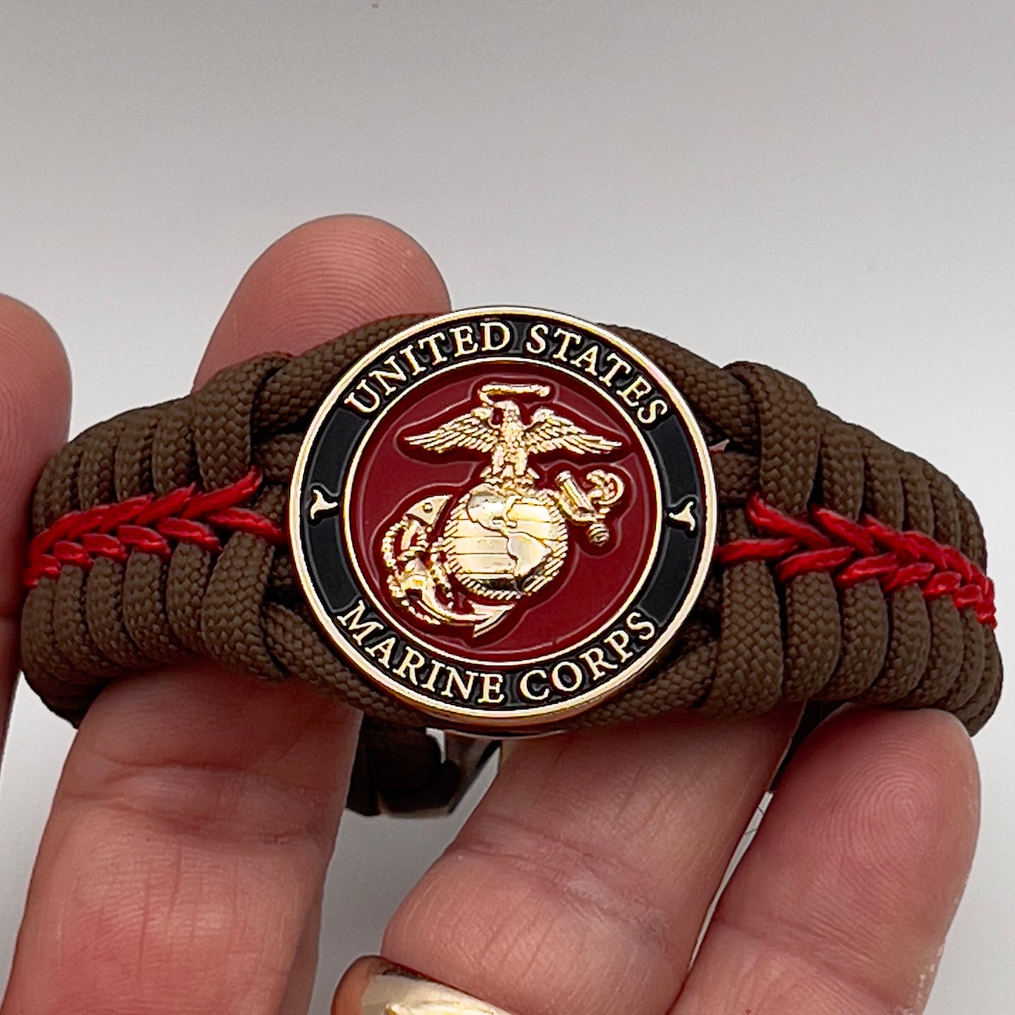 Thick, rigid and comfortable braided United States Marine Corps bracelet featuring a 24K gold plated USMC Eagle Globe and Anchor medallion, a gold Cobra style tactical buckle and woven with Coyote Brown 550 paracord and Imperial Red micro cord.