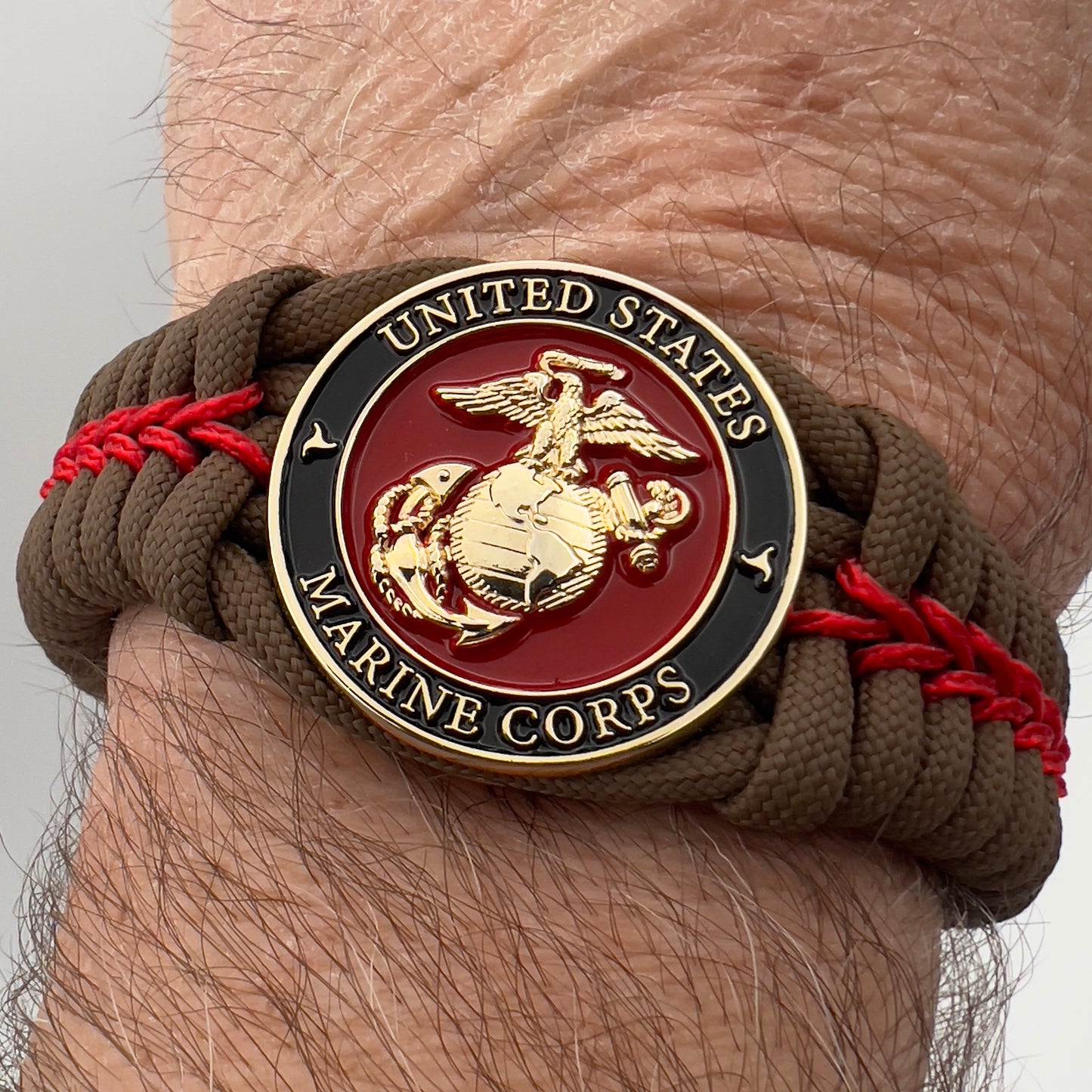 Thick, rigid and comfortable braided United States Marine Corps bracelet featuring a 24K gold plated USMC Eagle Globe and Anchor medallion, a gold Cobra style tactical buckle and woven with Coyote Brown 550 paracord and Imperial Red micro cord.