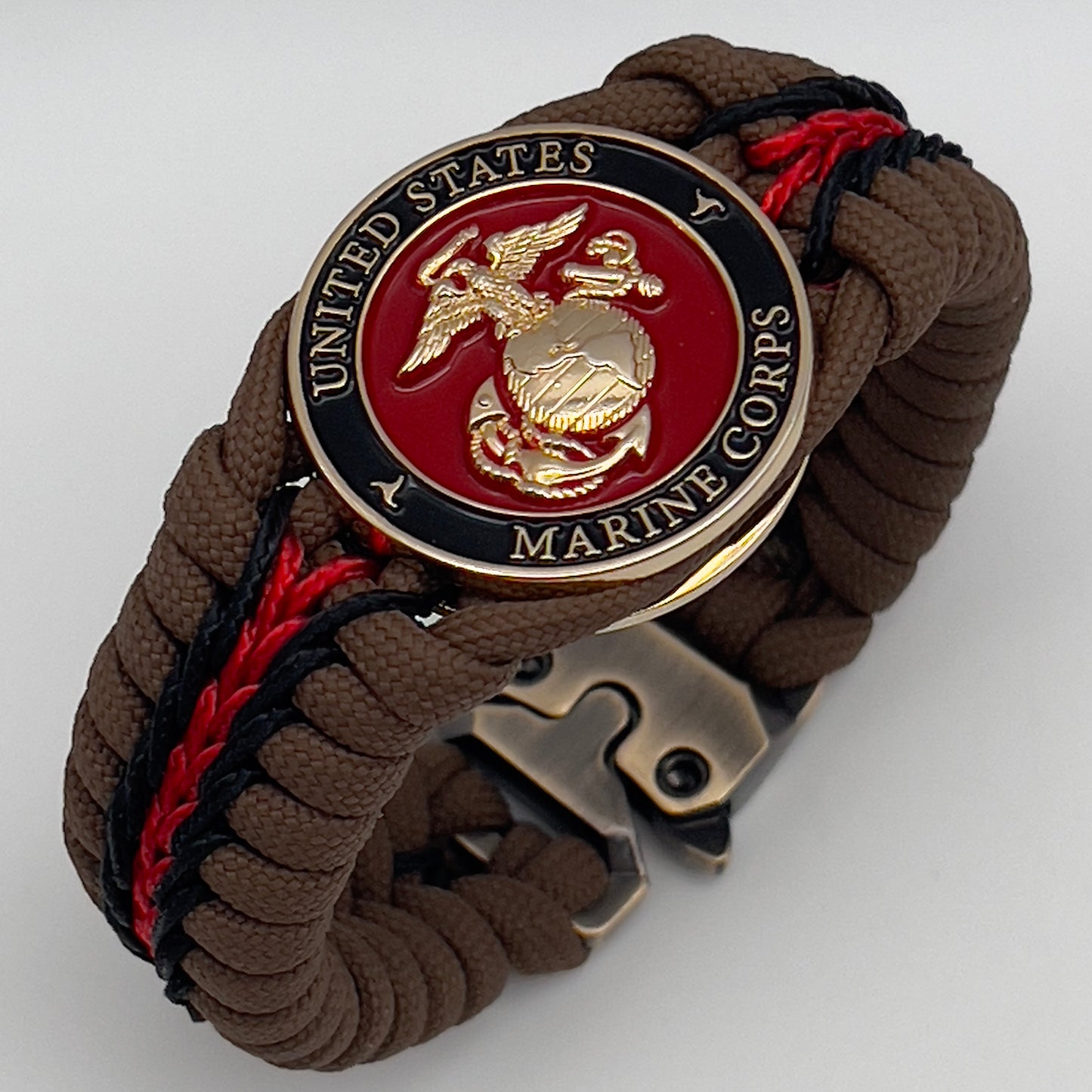 Thick, rigid and comfortable braided United States Marine Corps bracelet featuring a 24K gold plated USMC Eagle Globe and Anchor medallion, a gold Cobra style tactical buckle and woven with Coyote Brown 550 paracord and Imperial Red and black micro cord.
