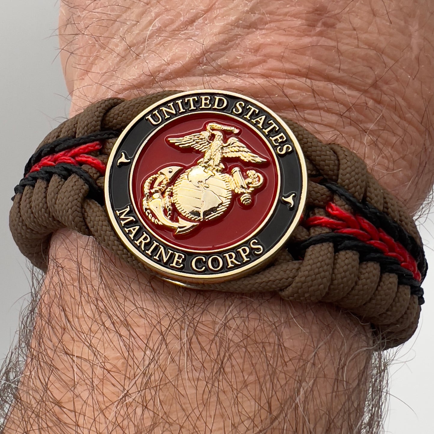 Thick, rigid and comfortable braided United States Marine Corps bracelet featuring a 24K gold plated USMC Eagle Globe and Anchor medallion, a gold Cobra style tactical buckle and woven with Coyote Brown 550 paracord and Imperial Red and black micro cord.
