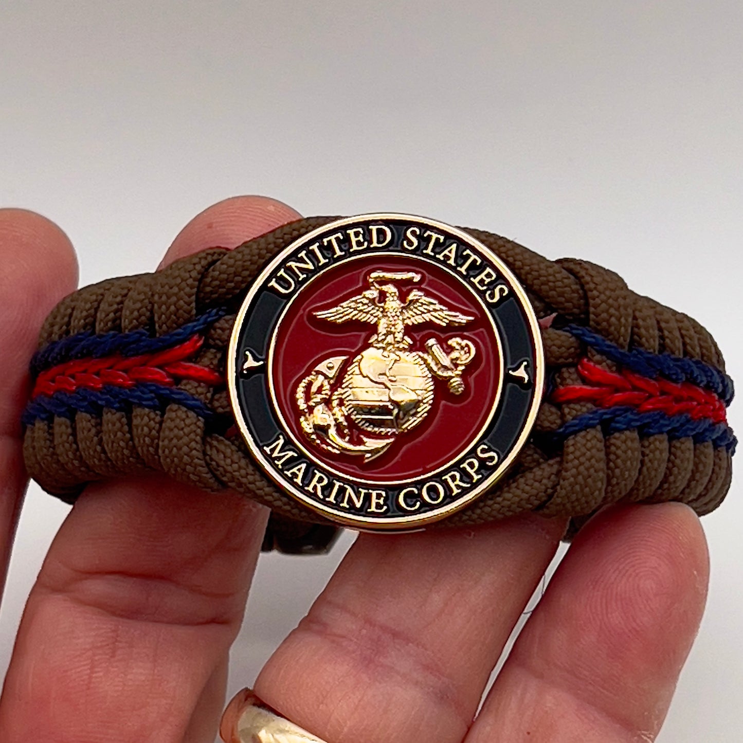 Thick, rigid and comfortable braided United States Marine Corps bracelet featuring a 24K gold plated USMC Eagle Globe and Anchor medallion, a gold Cobra style tactical buckle and woven with Coyote Brown 550 paracord and Imperial Red and Navy Blue micro cord.
