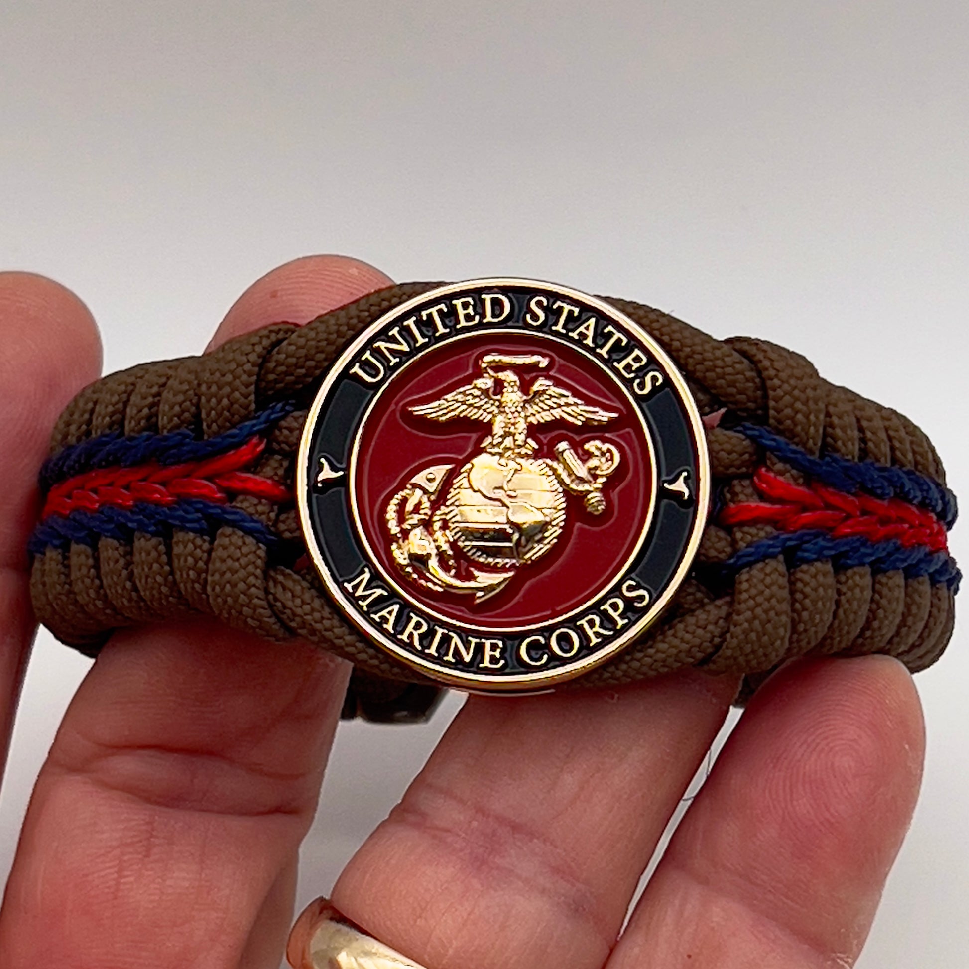 Thick, rigid and comfortable braided United States Marine Corps bracelet featuring a 24K gold plated USMC Eagle Globe and Anchor medallion, a gold Cobra style tactical buckle and woven with Coyote Brown 550 paracord and Imperial Red and Navy Blue micro cord.