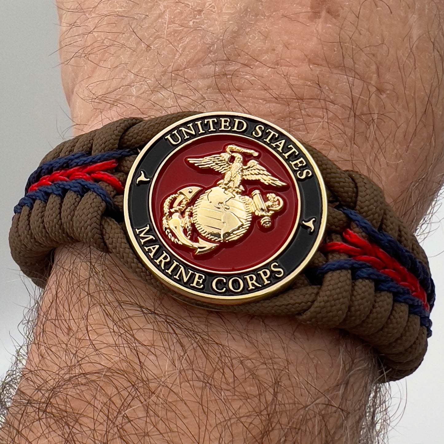 Thick, rigid and comfortable braided United States Marine Corps bracelet featuring a 24K gold plated USMC Eagle Globe and Anchor medallion, a gold Cobra style tactical buckle and woven with Coyote Brown 550 paracord and Imperial Red and Navy Blue micro cord.