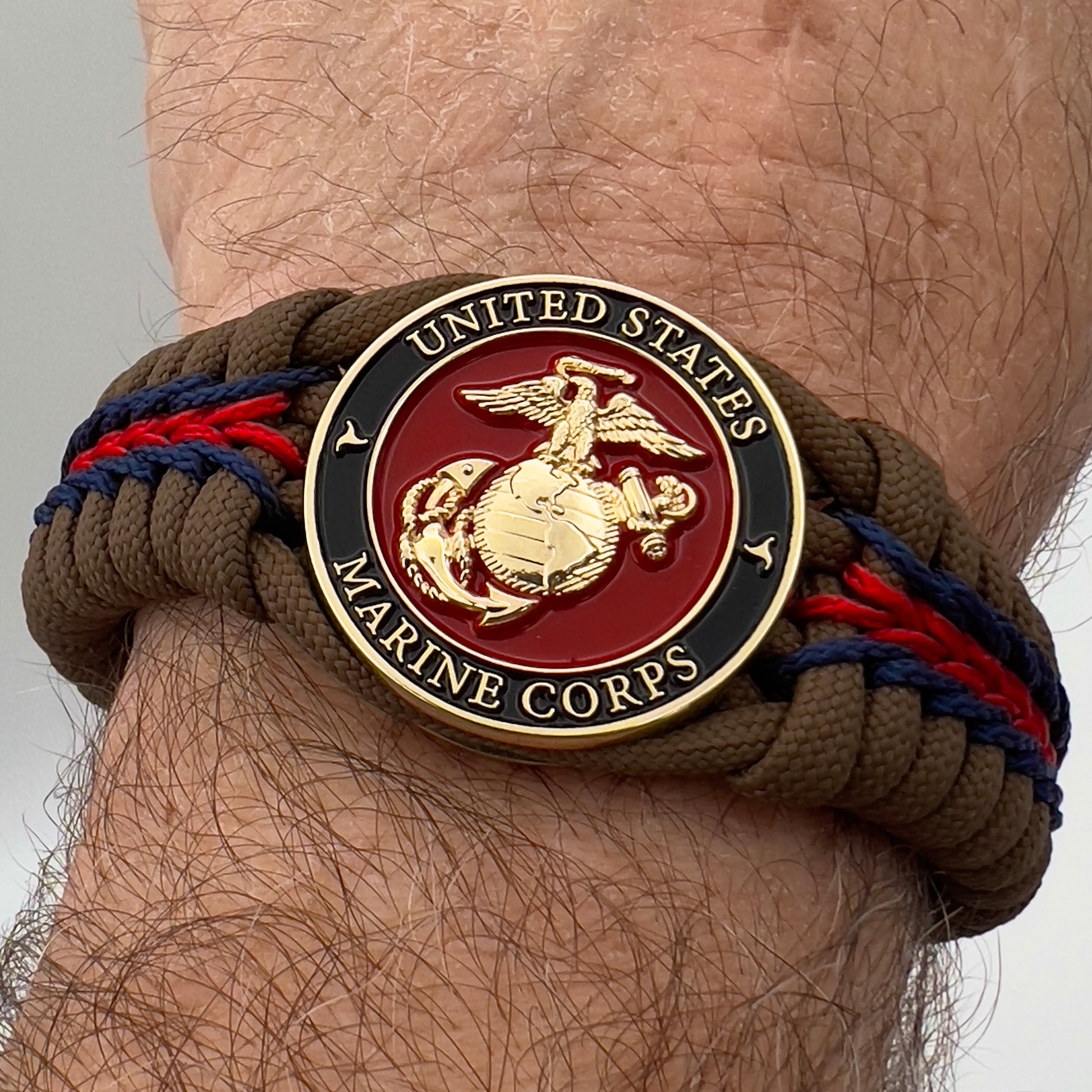 Thick, rigid and comfortable braided United States Marine Corps bracelet featuring a 24K gold plated USMC Eagle Globe and Anchor medallion, a gold Cobra style tactical buckle and woven with Coyote Brown 550 paracord and Imperial Red and Navy Blue micro cord.