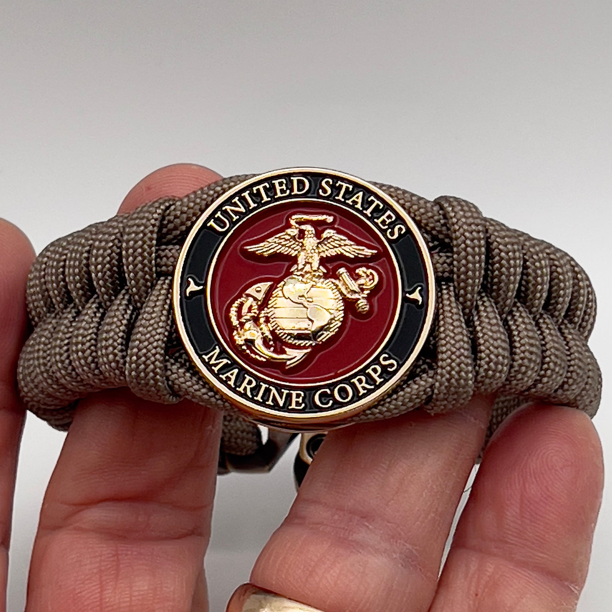 Thick, semi-rigid and comfortable braided United States Marine Corps bracelet featuring a 24K gold plated USMC Eagle Globe and Anchor medallion, a gold Cobra style tactical buckle and woven with tan 550 paracord.