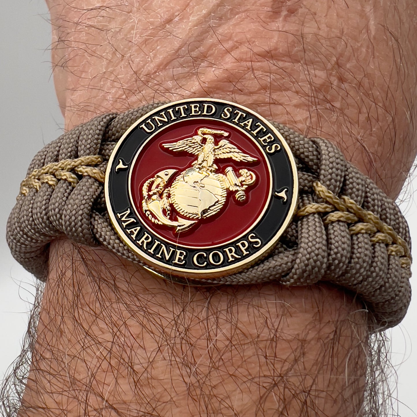 Thick, semi-rigid and comfortable braided United States Marine Corps bracelet featuring a 24K gold plated USMC Eagle Globe and Anchor medallion, a gold Cobra style tactical buckle and woven with tan 550 paracord and gold micro cord.