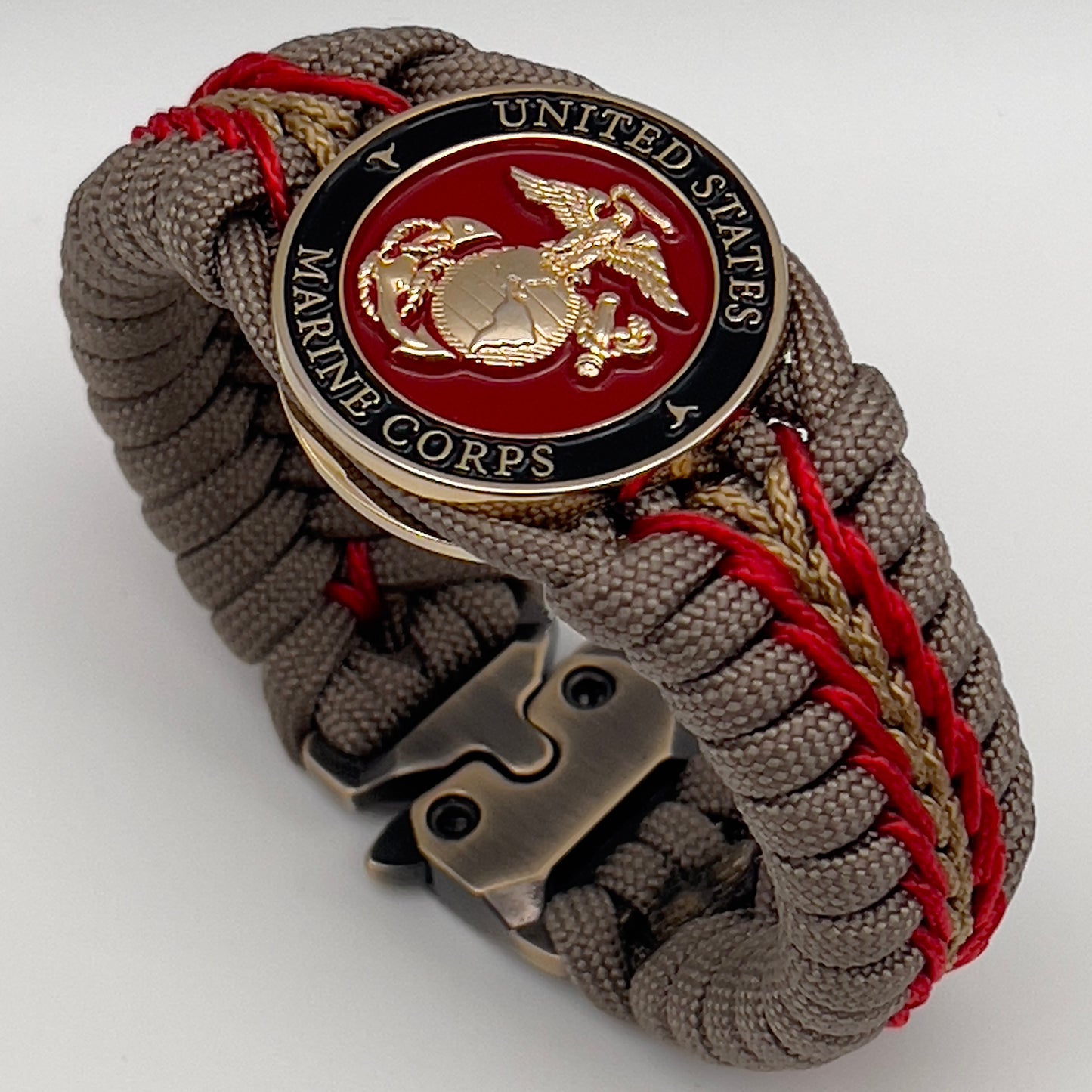 Thick, rigid and comfortable braided United States Marine Corps bracelet featuring a 24K gold plated USMC Eagle Globe and Anchor medallion, a gold Cobra style tactical buckle and woven with tan 550 paracord and Imperial Red and gold micro cord.