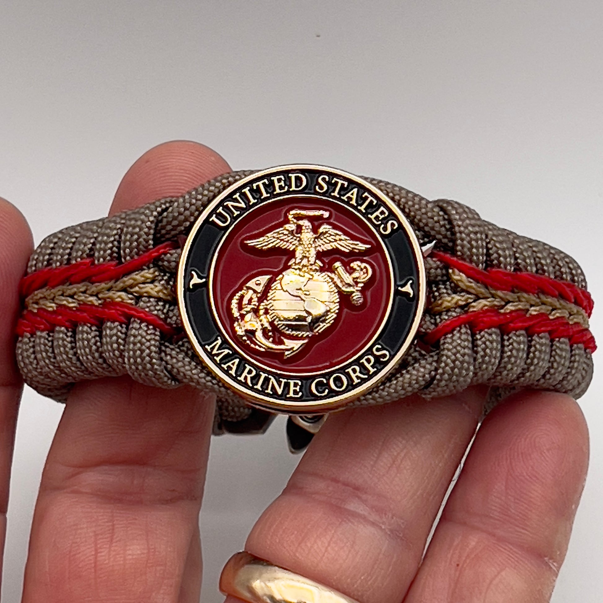 Thick, rigid and comfortable braided United States Marine Corps bracelet featuring a 24K gold plated USMC Eagle Globe and Anchor medallion, a gold Cobra style tactical buckle and woven with tan 550 paracord and Imperial Red and gold micro cord.
