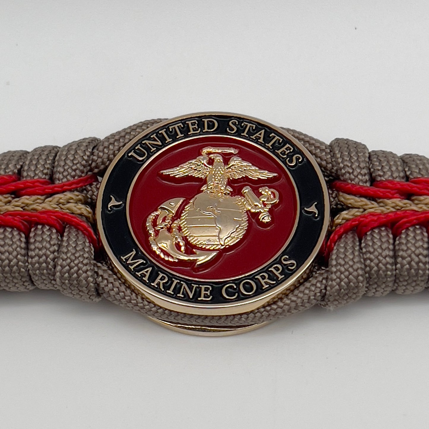 Thick, rigid and comfortable braided United States Marine Corps bracelet featuring a 24K gold plated USMC Eagle Globe and Anchor medallion, a gold Cobra style tactical buckle and woven with tan 550 paracord and Imperial Red and gold micro cord.