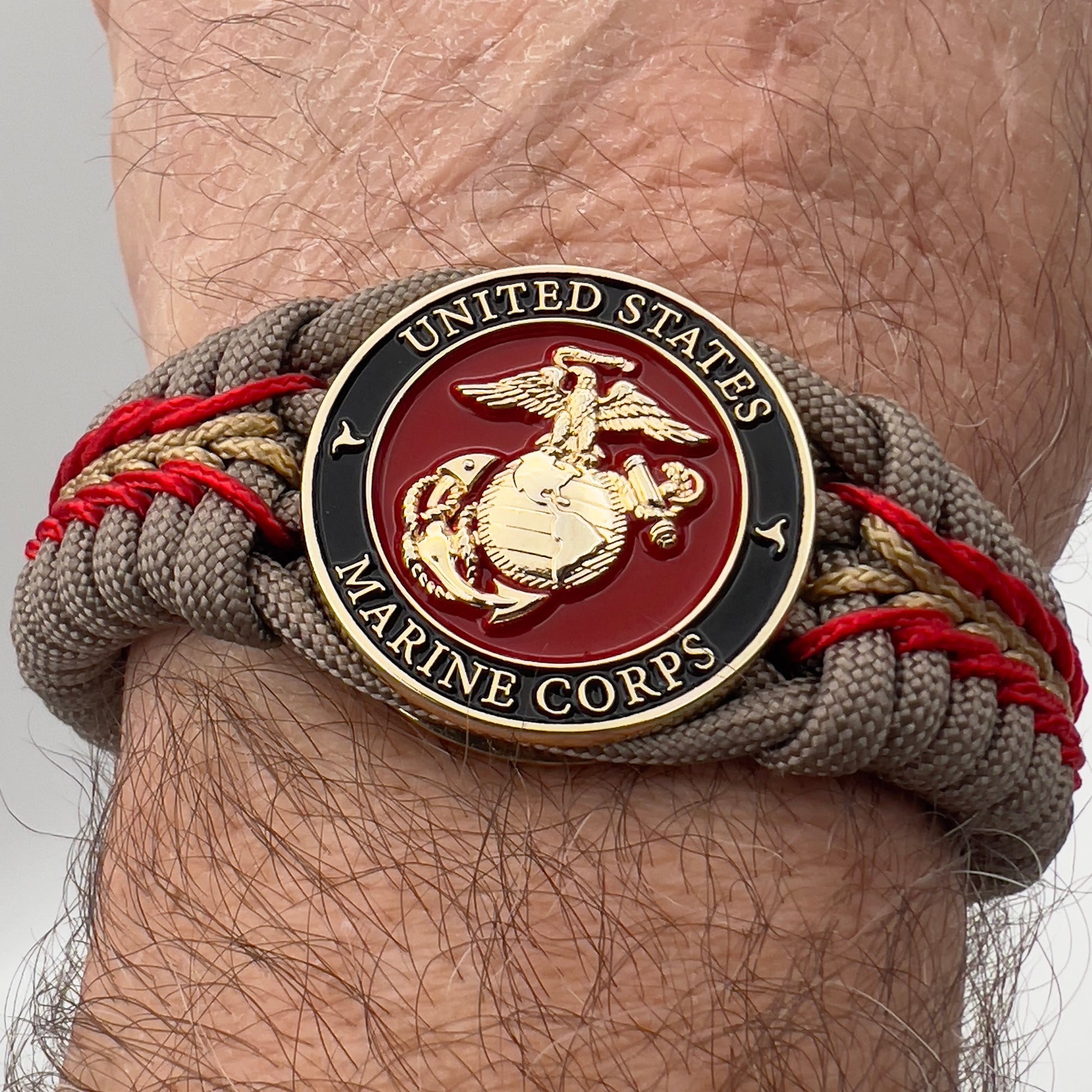 Thick, rigid and comfortable braided United States Marine Corps bracelet featuring a 24K gold plated USMC Eagle Globe and Anchor medallion, a gold Cobra style tactical buckle and woven with tan 550 paracord and Imperial Red and gold micro cord.