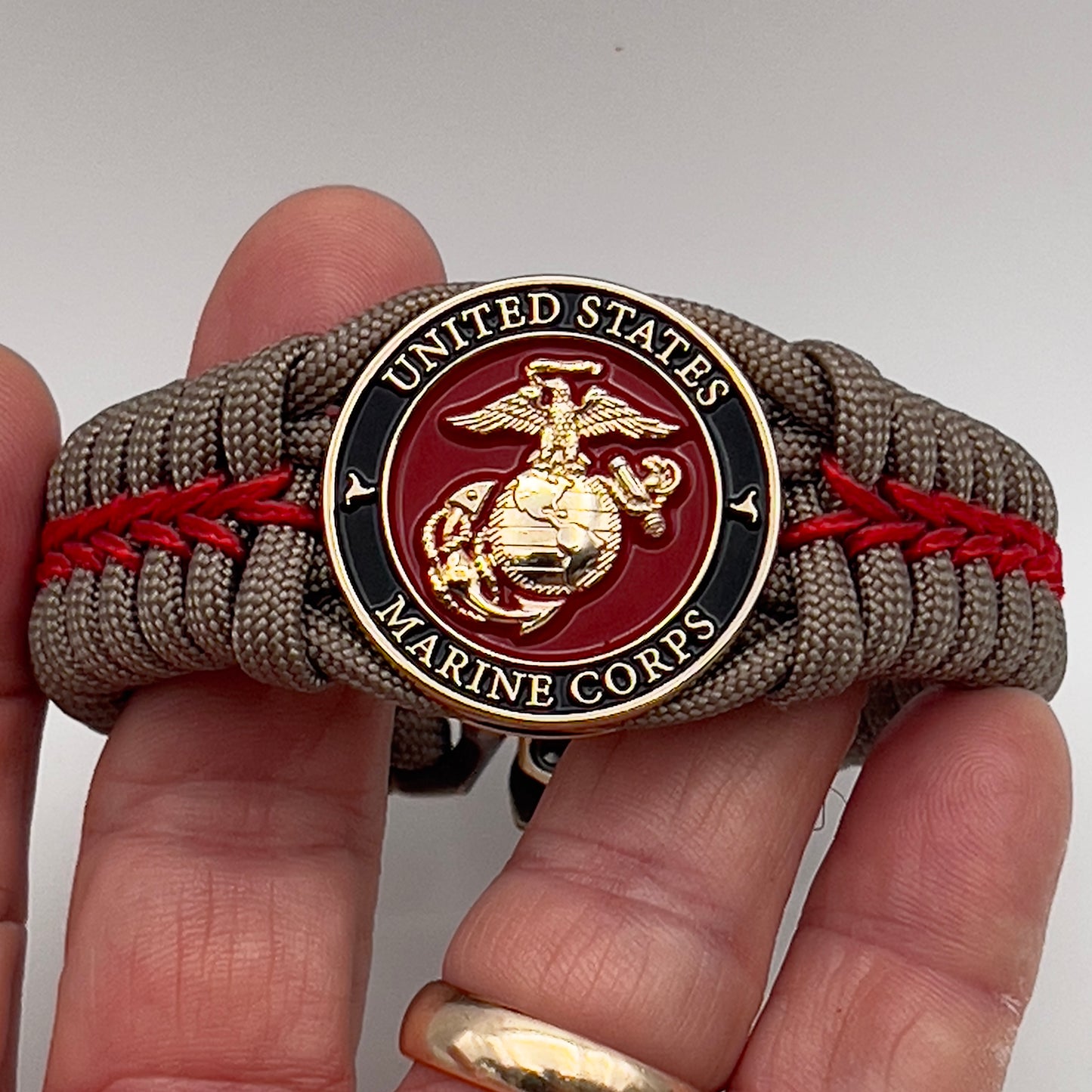 Thick, rigid and comfortable braided United States Marine Corps bracelet featuring a 24K gold plated USMC Eagle Globe and Anchor medallion, a gold Cobra style tactical buckle and woven with tan 550 paracord and Imperial Red micro cord.