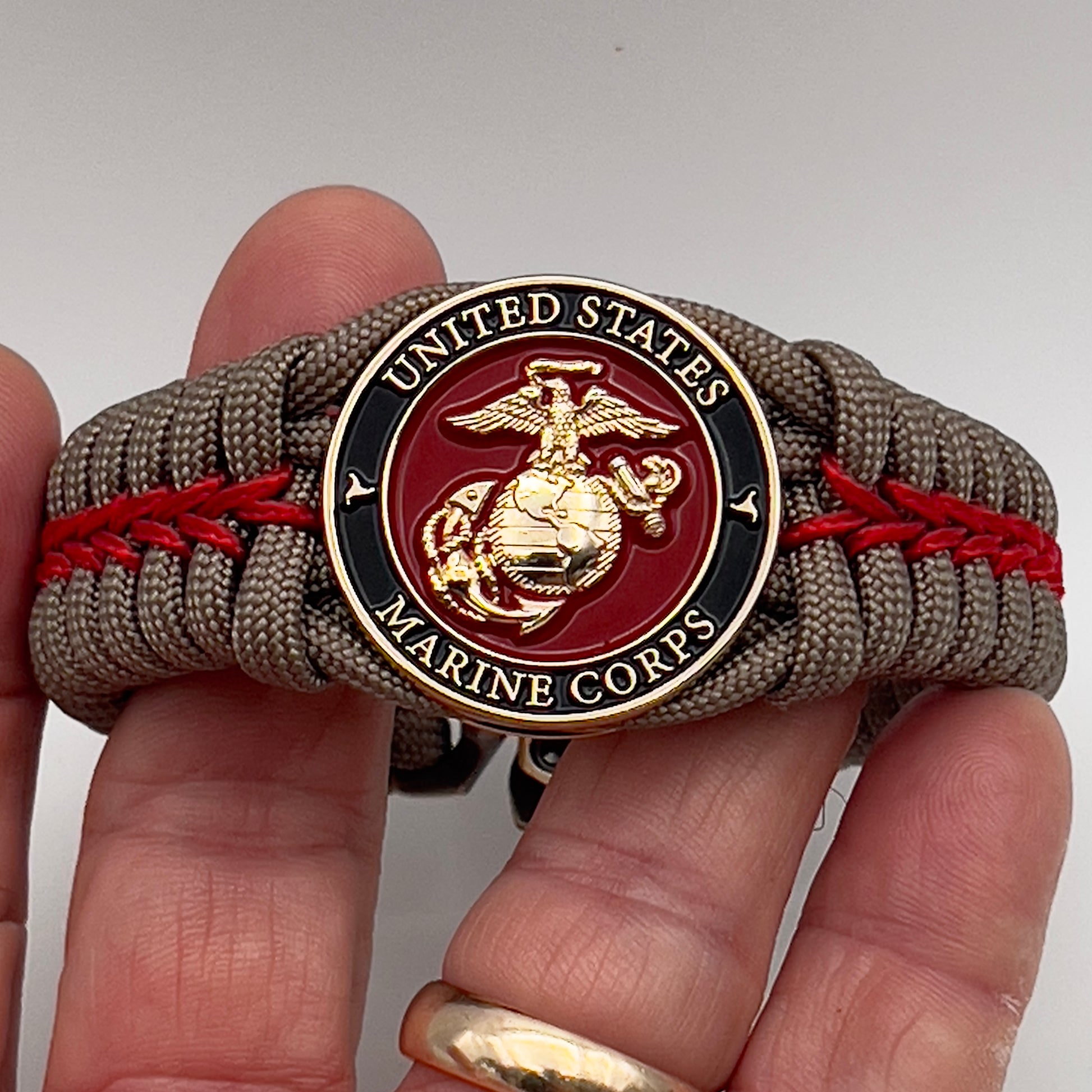 Thick, rigid and comfortable braided United States Marine Corps bracelet featuring a 24K gold plated USMC Eagle Globe and Anchor medallion, a gold Cobra style tactical buckle and woven with tan 550 paracord and Imperial Red micro cord.