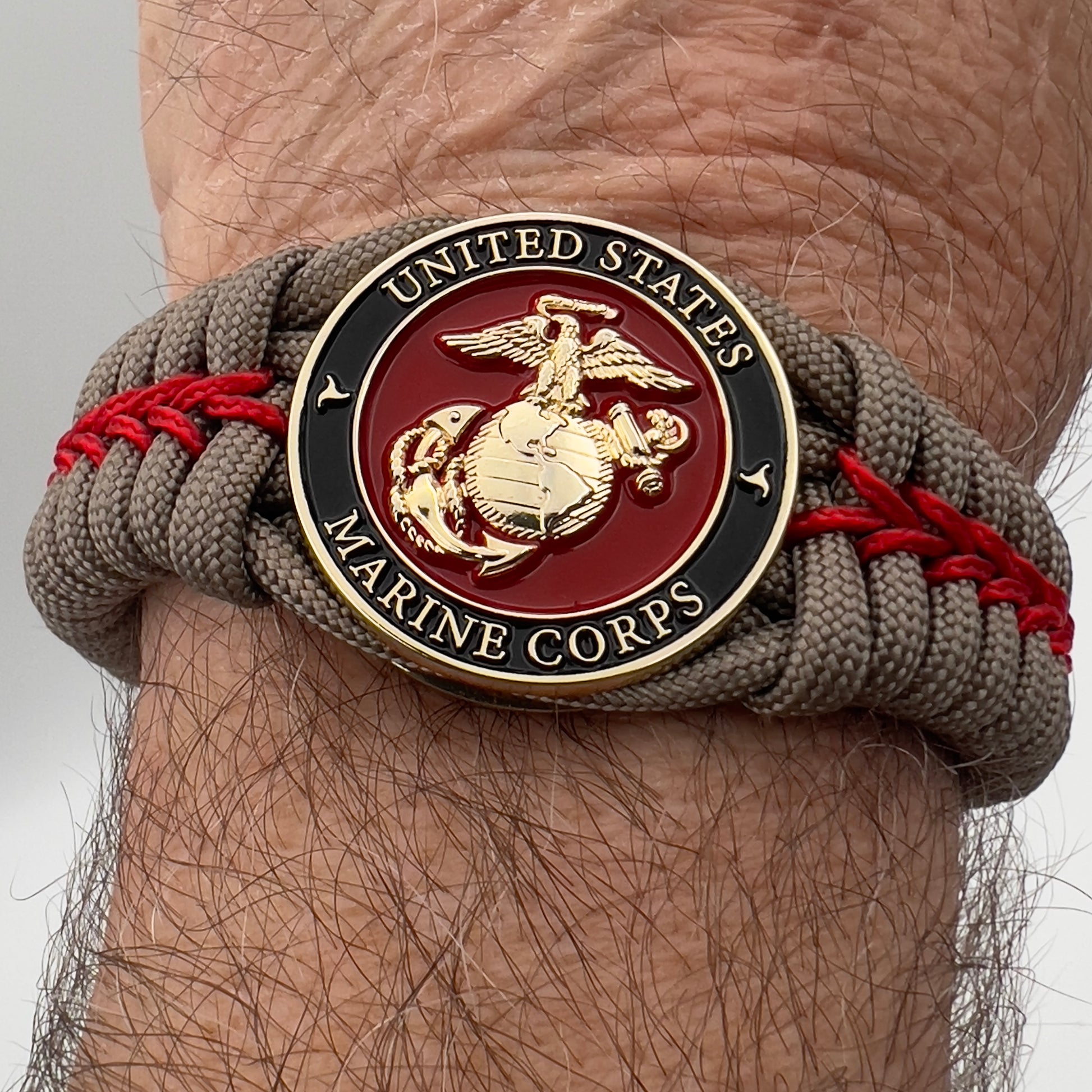 Thick, rigid and comfortable braided United States Marine Corps bracelet featuring a 24K gold plated USMC Eagle Globe and Anchor medallion, a gold Cobra style tactical buckle and woven with tan 550 paracord and Imperial Red micro cord.