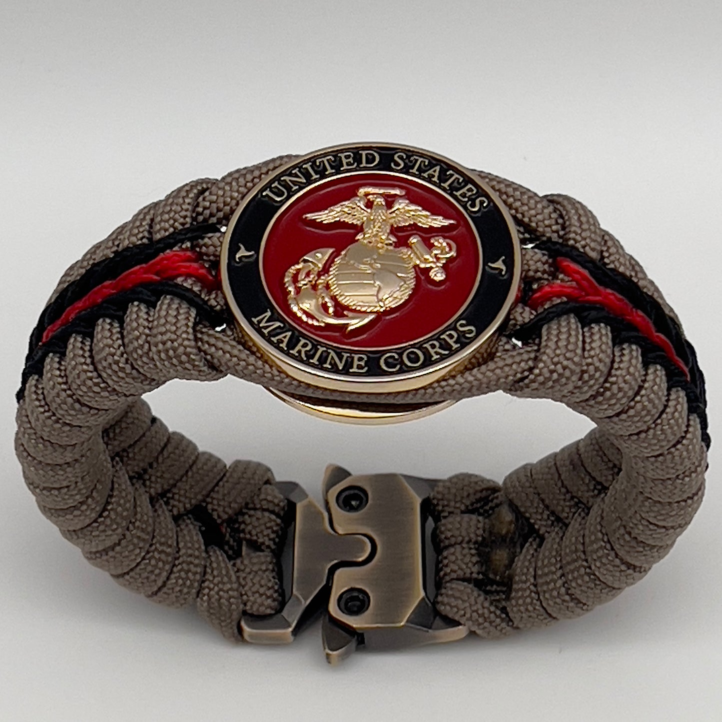 Thick, rigid and comfortable braided United States Marine Corps bracelet featuring a 24K gold plated USMC Eagle Globe and Anchor medallion, a gold Cobra style tactical buckle and woven with tan 550 paracord and Imperial Red and black micro cord.