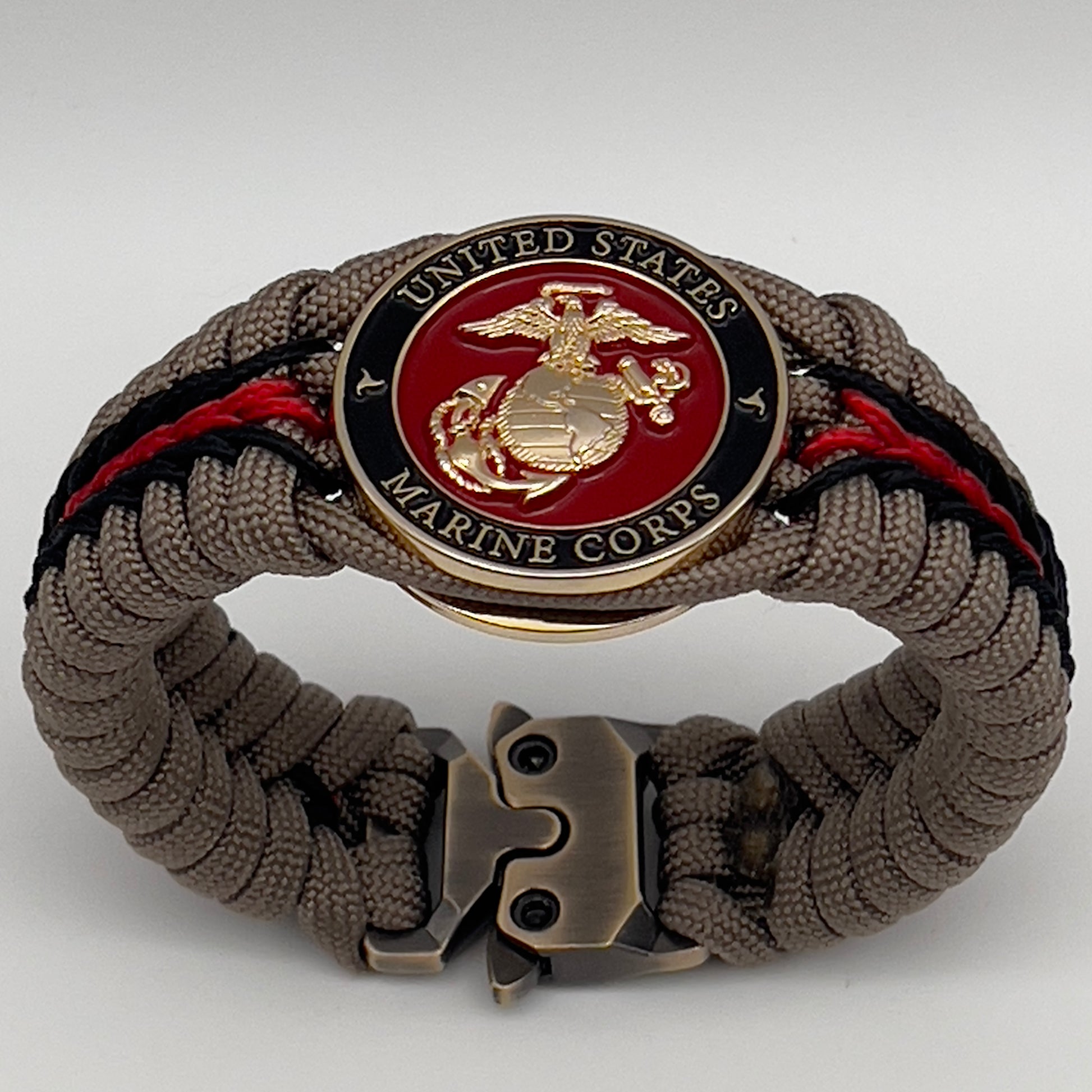 Thick, rigid and comfortable braided United States Marine Corps bracelet featuring a 24K gold plated USMC Eagle Globe and Anchor medallion, a gold Cobra style tactical buckle and woven with tan 550 paracord and Imperial Red and black micro cord.
