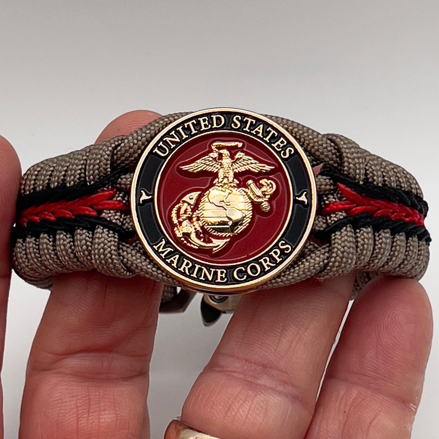 Thick, rigid and comfortable braided United States Marine Corps bracelet featuring a 24K gold plated USMC Eagle Globe and Anchor medallion, a gold Cobra style tactical buckle and woven with tan 550 paracord and Imperial Red and black micro cord.