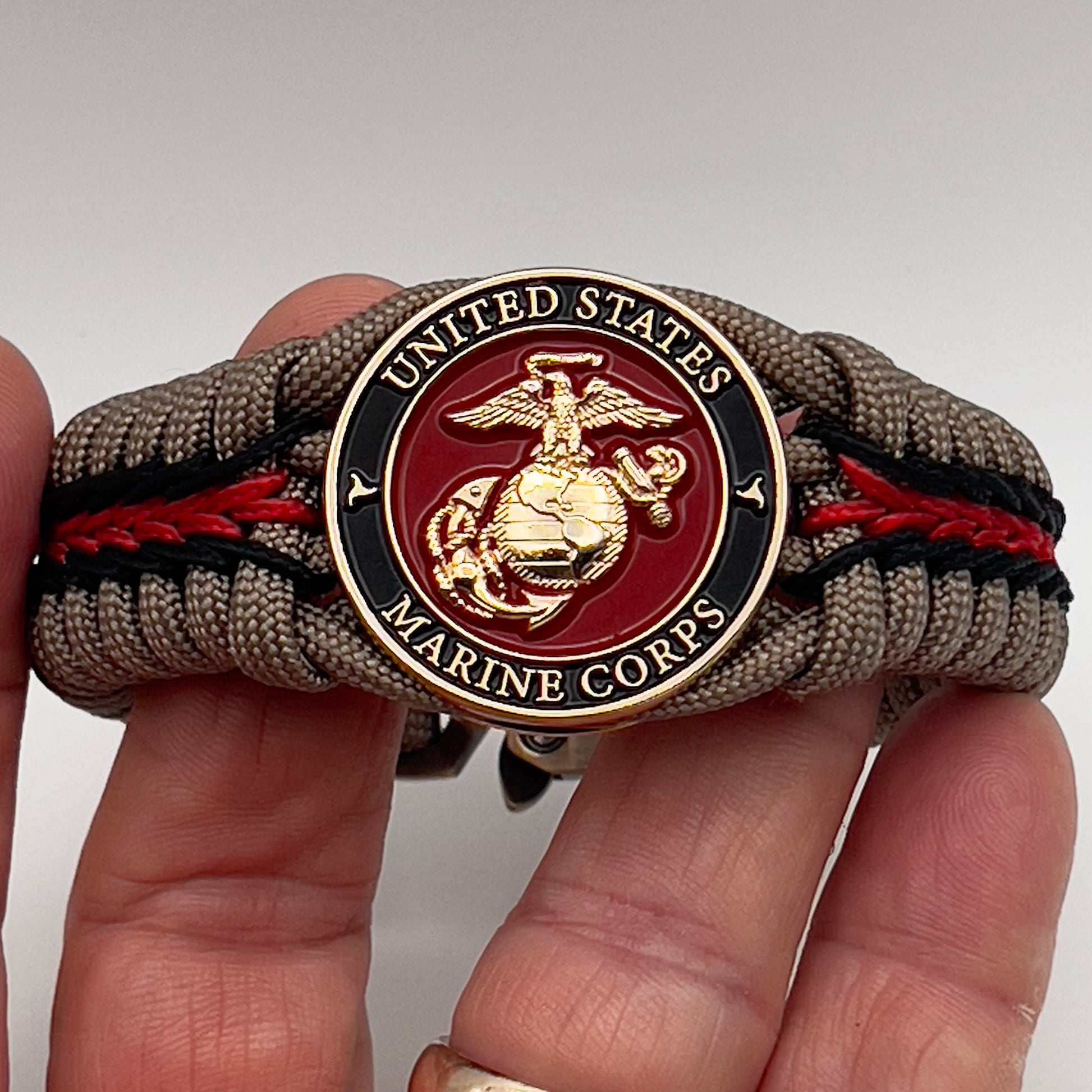 Thick, rigid and comfortable braided United States Marine Corps bracelet featuring a 24K gold plated USMC Eagle Globe and Anchor medallion, a gold Cobra style tactical buckle and woven with tan 550 paracord and Imperial Red and black micro cord.