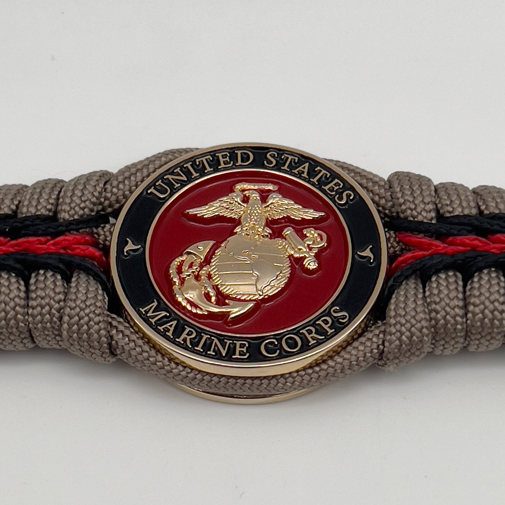 Thick, rigid and comfortable braided United States Marine Corps bracelet featuring a 24K gold plated USMC Eagle Globe and Anchor medallion, a gold Cobra style tactical buckle and woven with tan 550 paracord and Imperial Red and black micro cord.